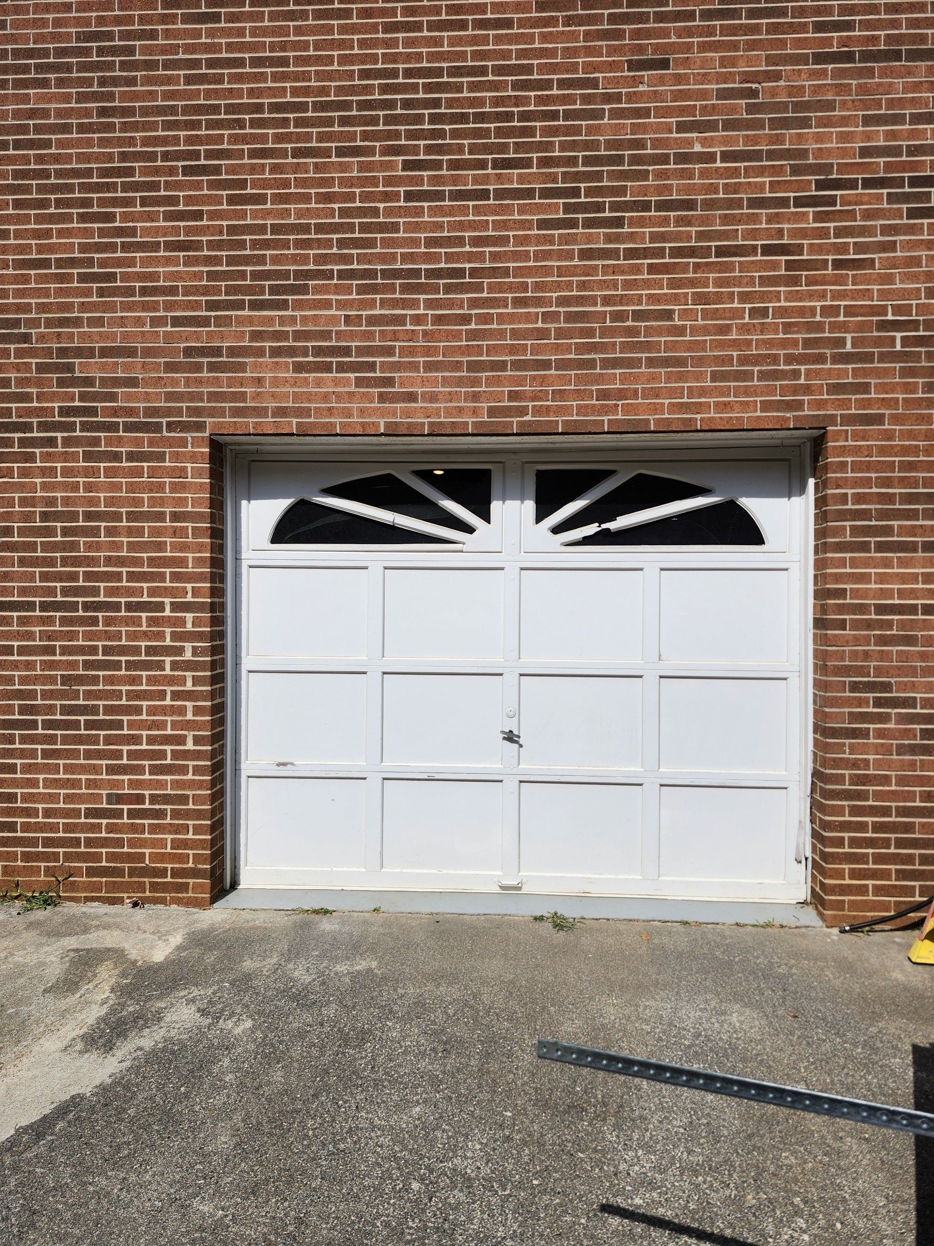 White garage door with arched window on a brick building; concrete driveway in front.