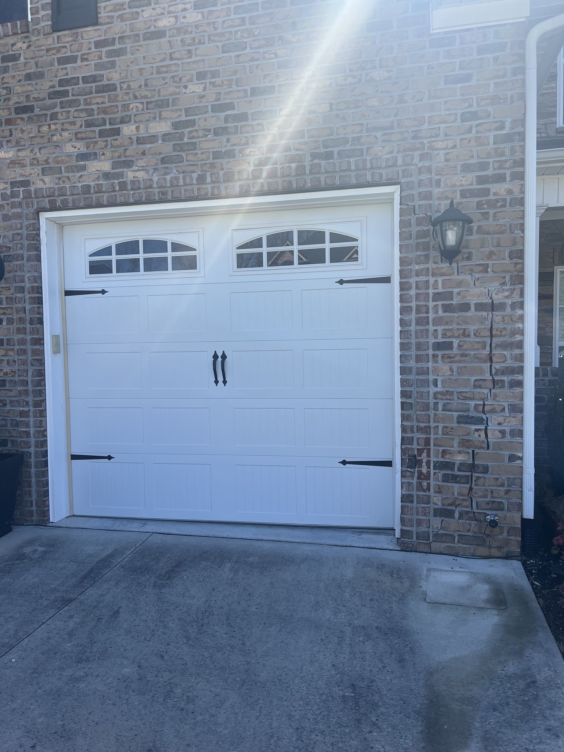 White garage door with arched windows and black hardware, set in a brick building.