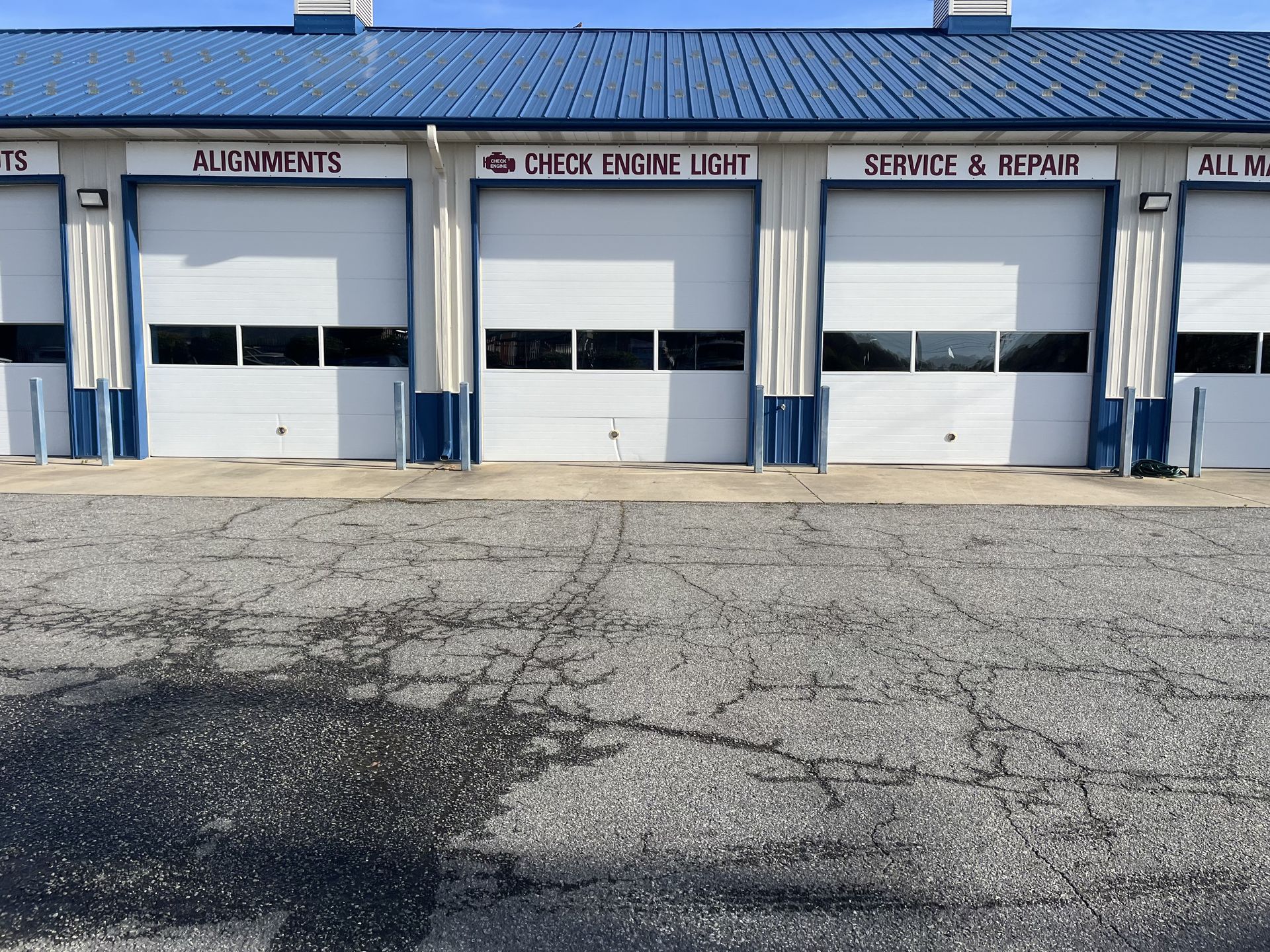 Exterior of an auto repair shop with four garage doors. Signs indicate alignments, wheel alignments, service & repair. Blue roof.