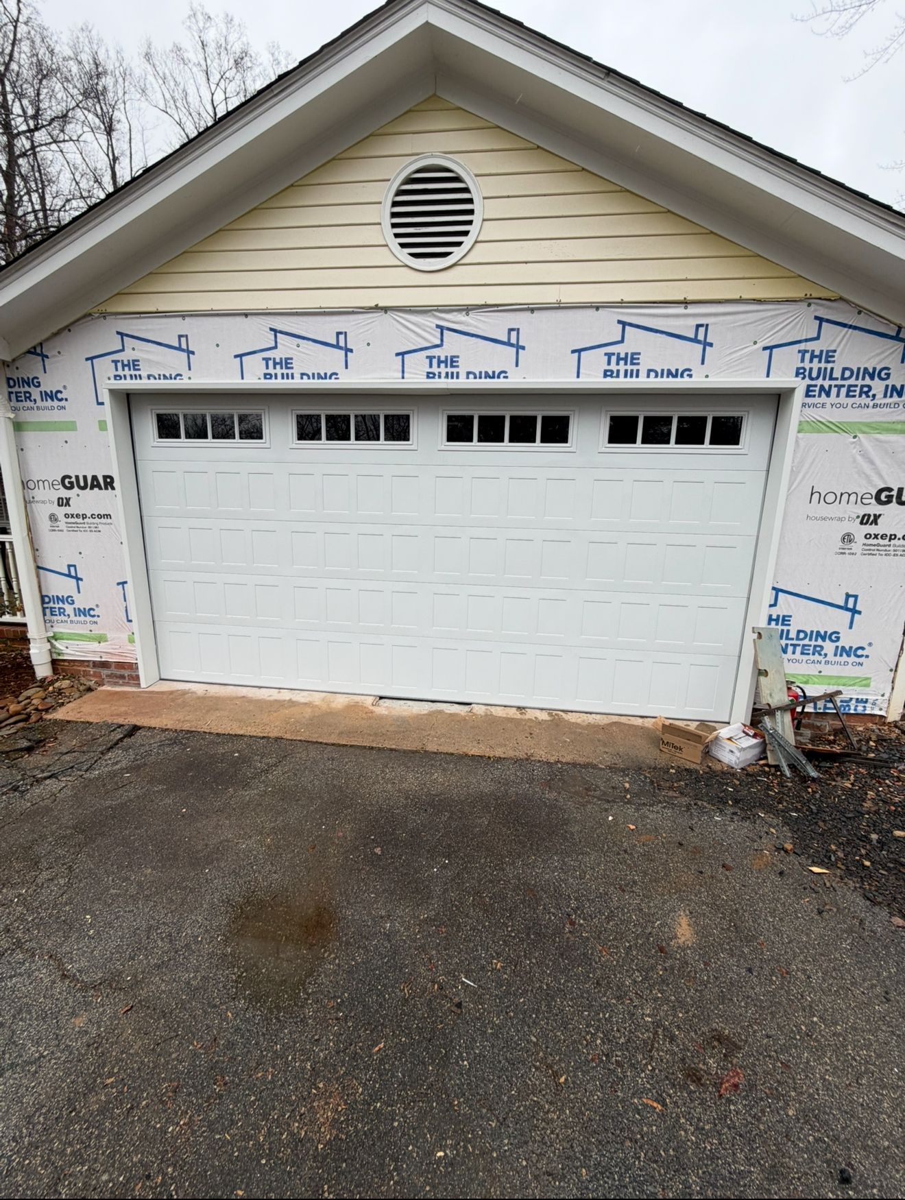 White garage door with windows, on a building with yellow siding and a dark driveway.