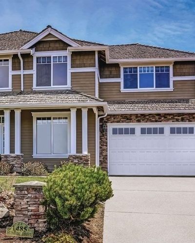 Tan house with white trim, stone accents, and a garage under a blue sky.