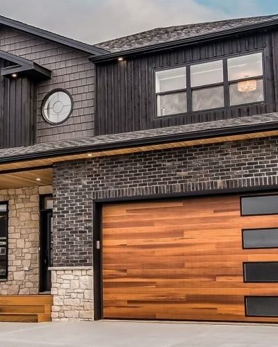 Two-story modern home with wood garage door, brick and dark siding, and round window.