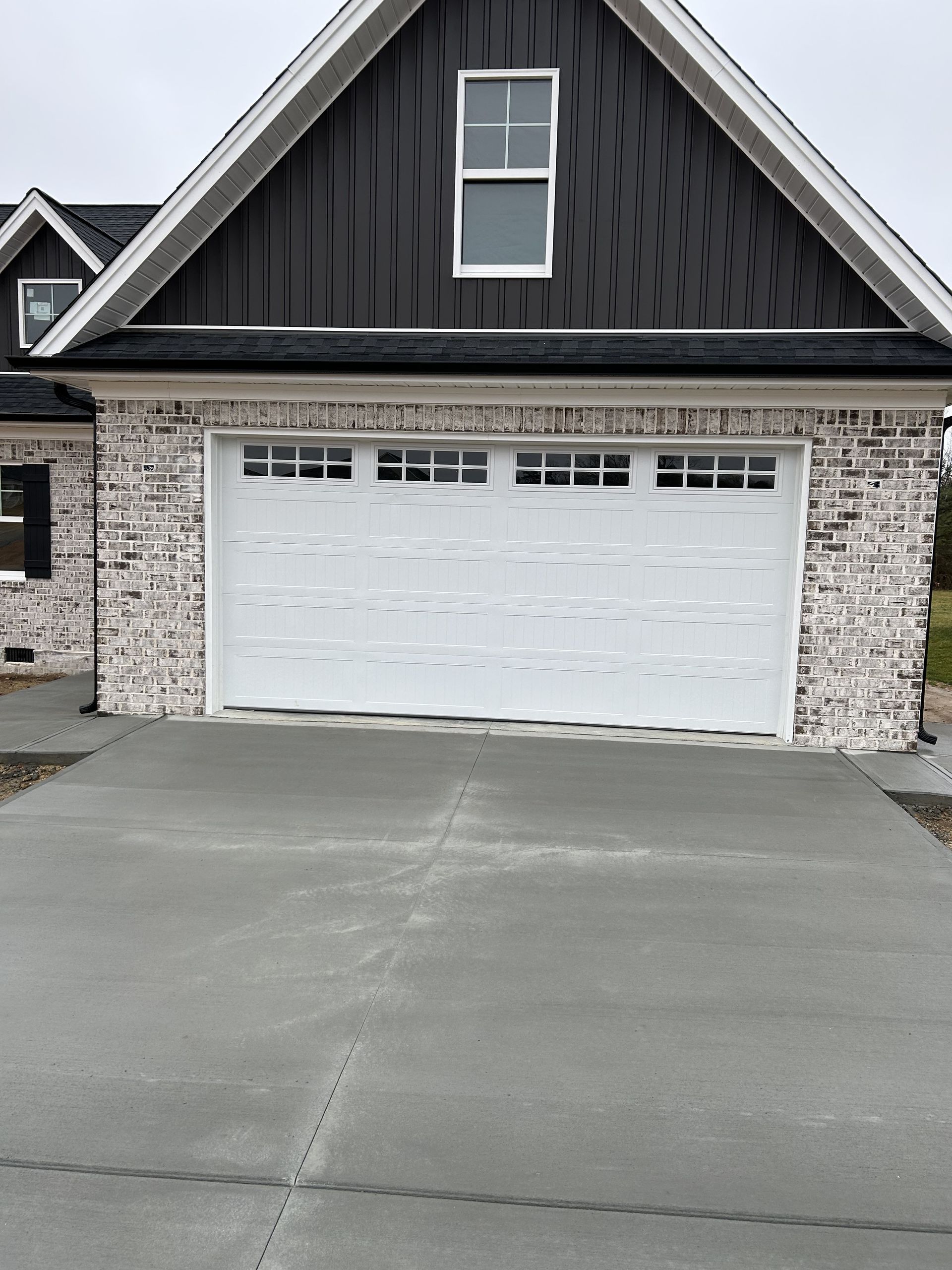 White garage door with brick facade, under a gray roof, in front of a concrete driveway.