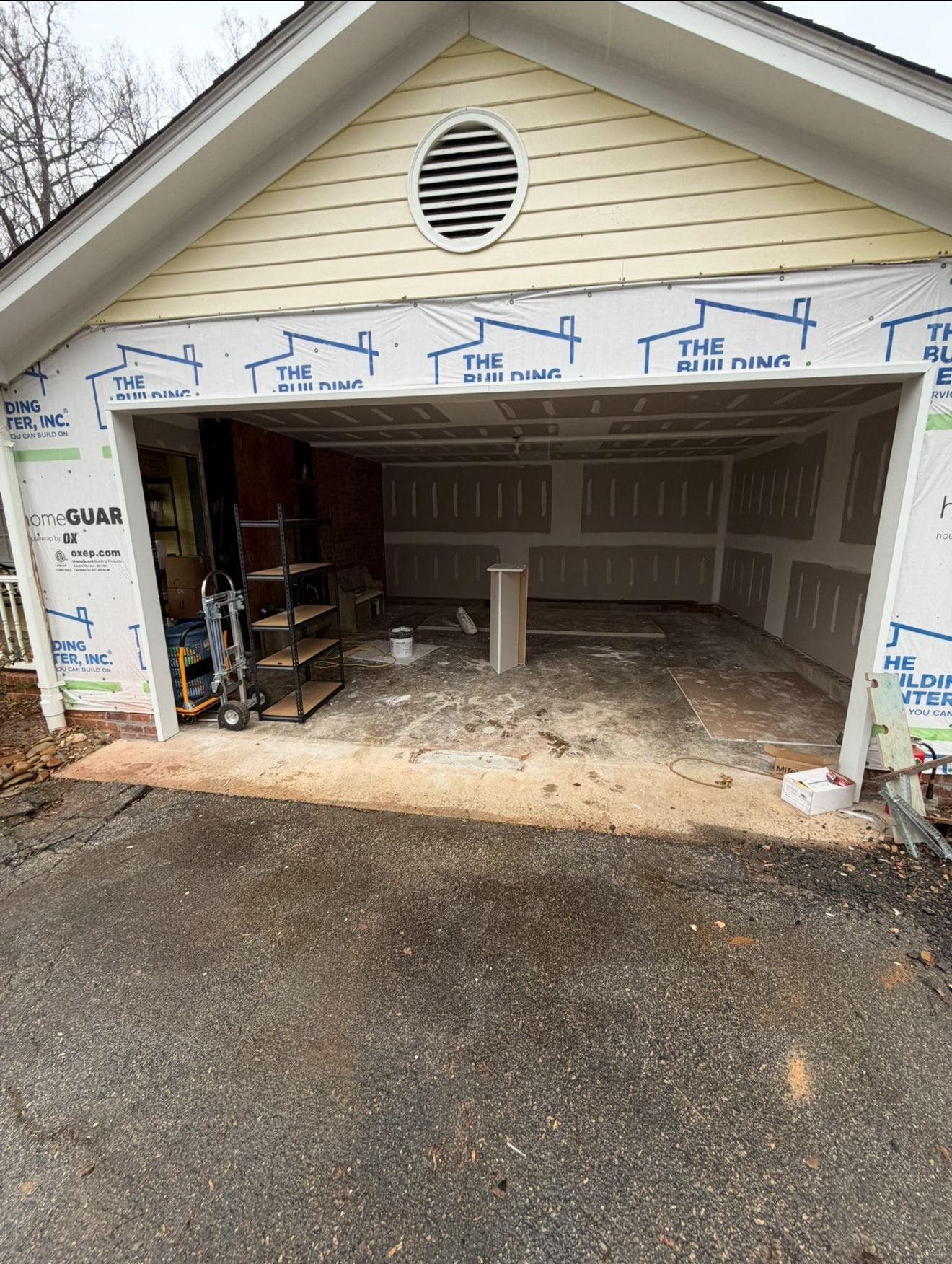Garage under construction; interior walls covered in drywall, exterior walls wrapped in blue paper. Asphalt driveway.