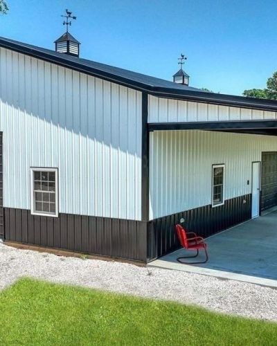 White and black barn with two cupolas topped with weather vanes, a red chair outside.