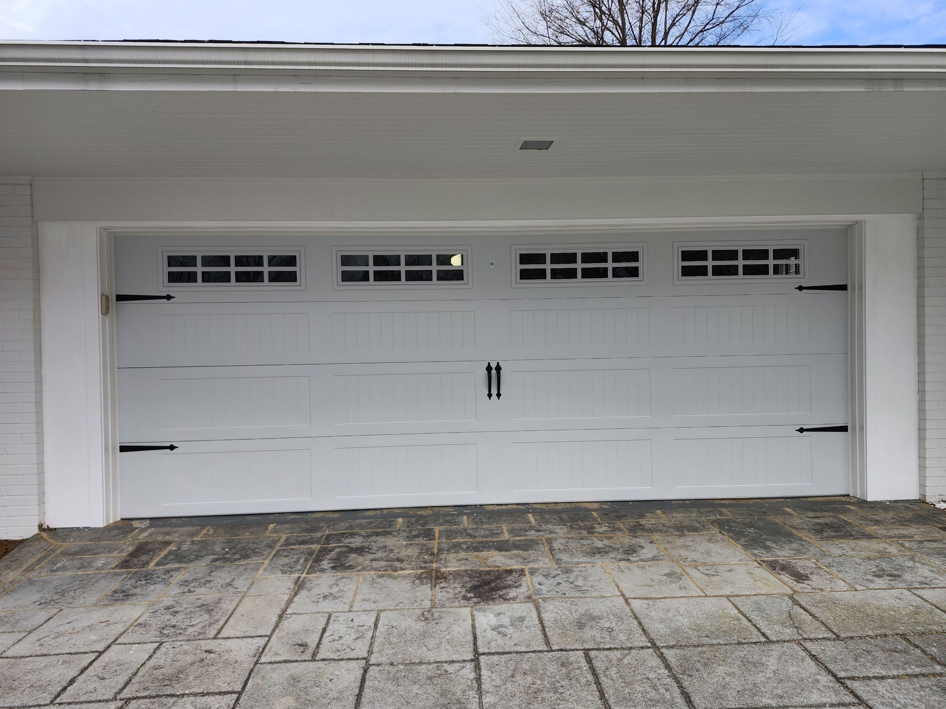 White garage door with decorative hardware on a brick patio.