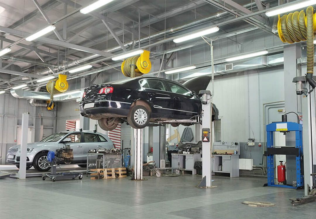 Car repair shop with two cars on lifts. One black, one silver. Tools and equipment visible.