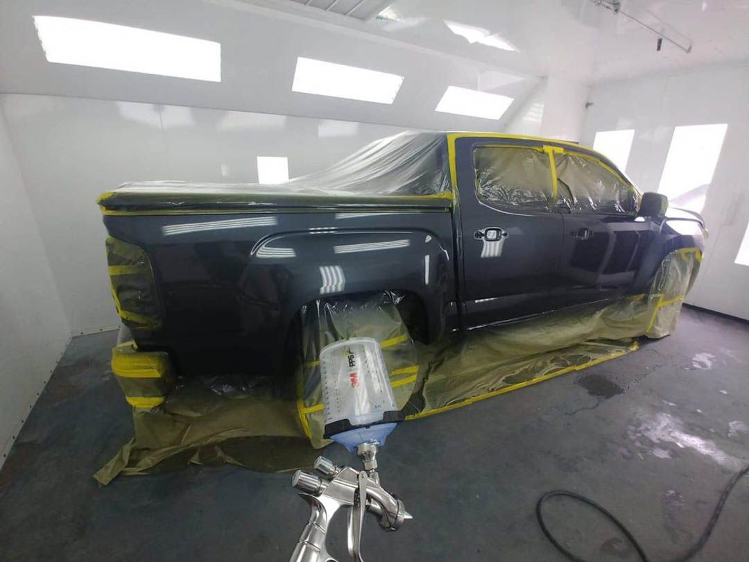 A pickup truck in a paint booth being sprayed with a dark grey paint.