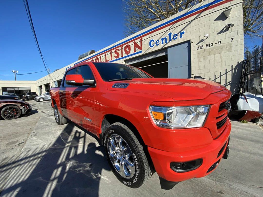 Red Dodge Ram pickup truck in front of a collision center on a sunny day.