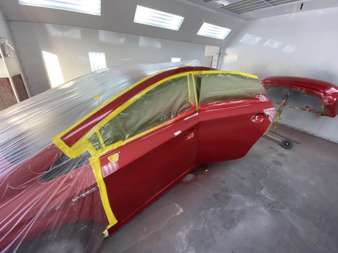 Red car door taped for painting inside a paint booth.