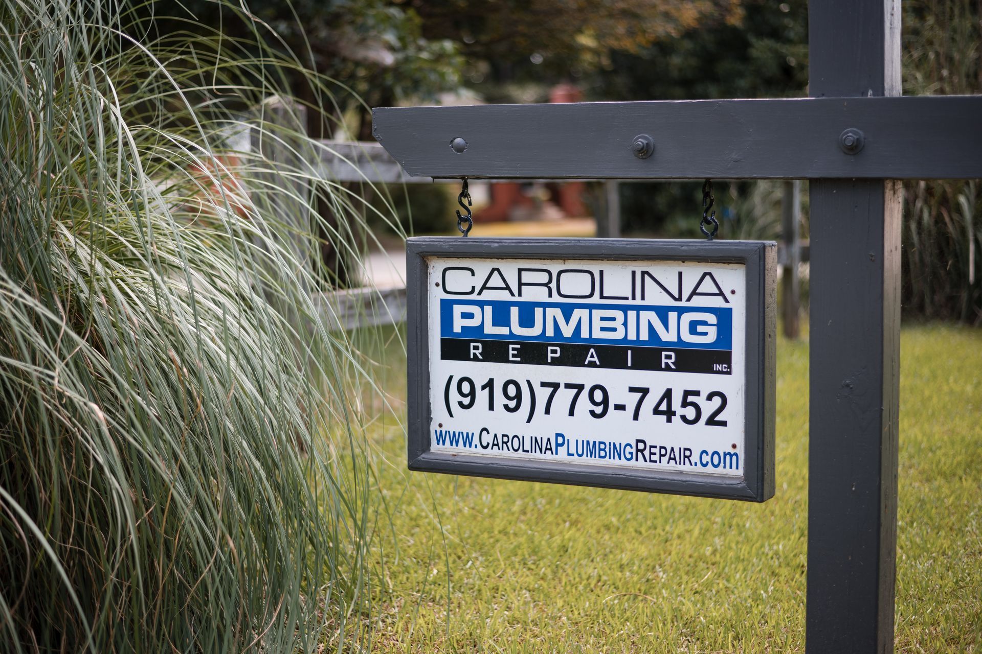 Carolina Plumbing yard sign hanging by a roadside, with phone number 919-779-7452.