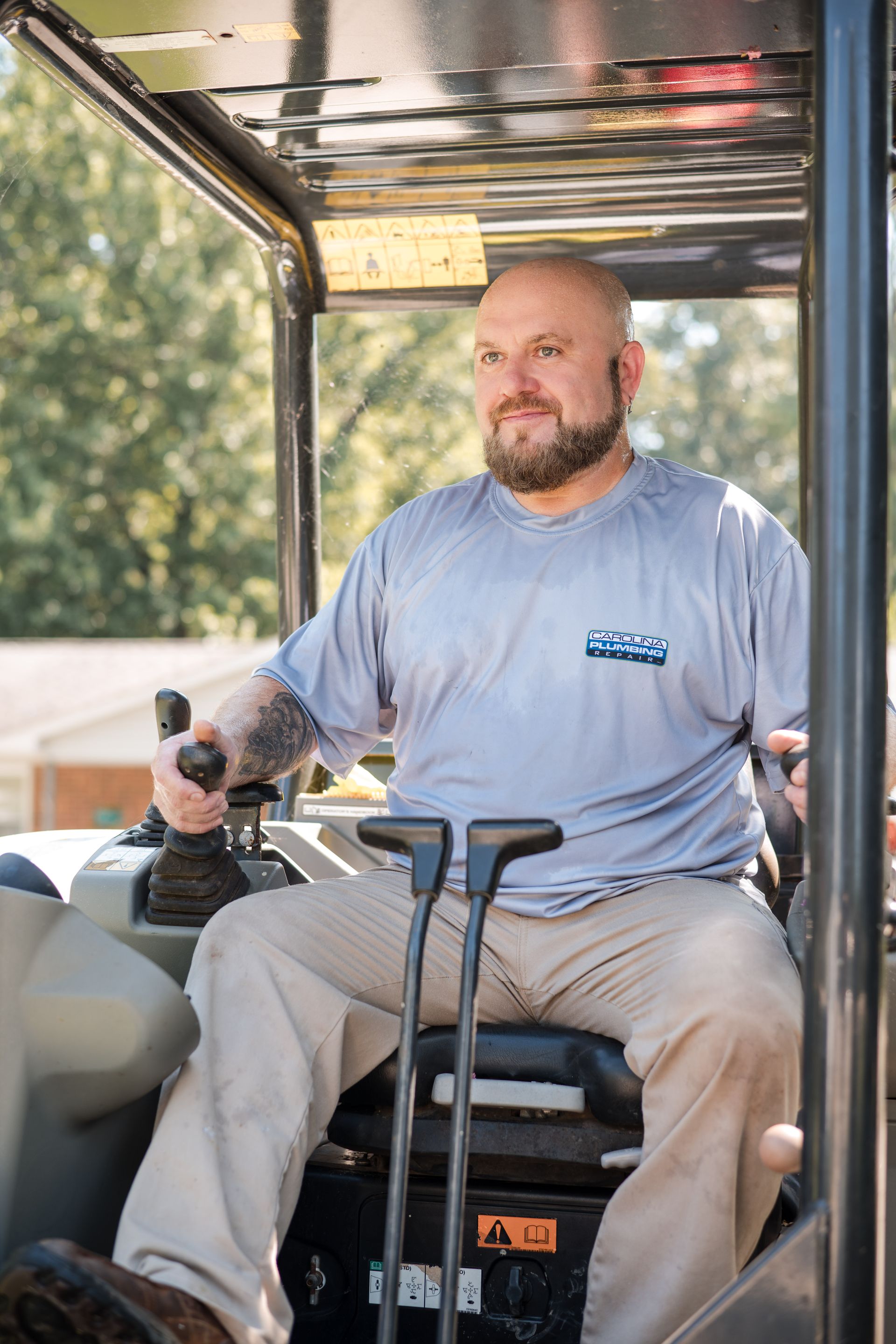 Man sitting on a small tractor, holding the controls, under a metal canopy outdoors.