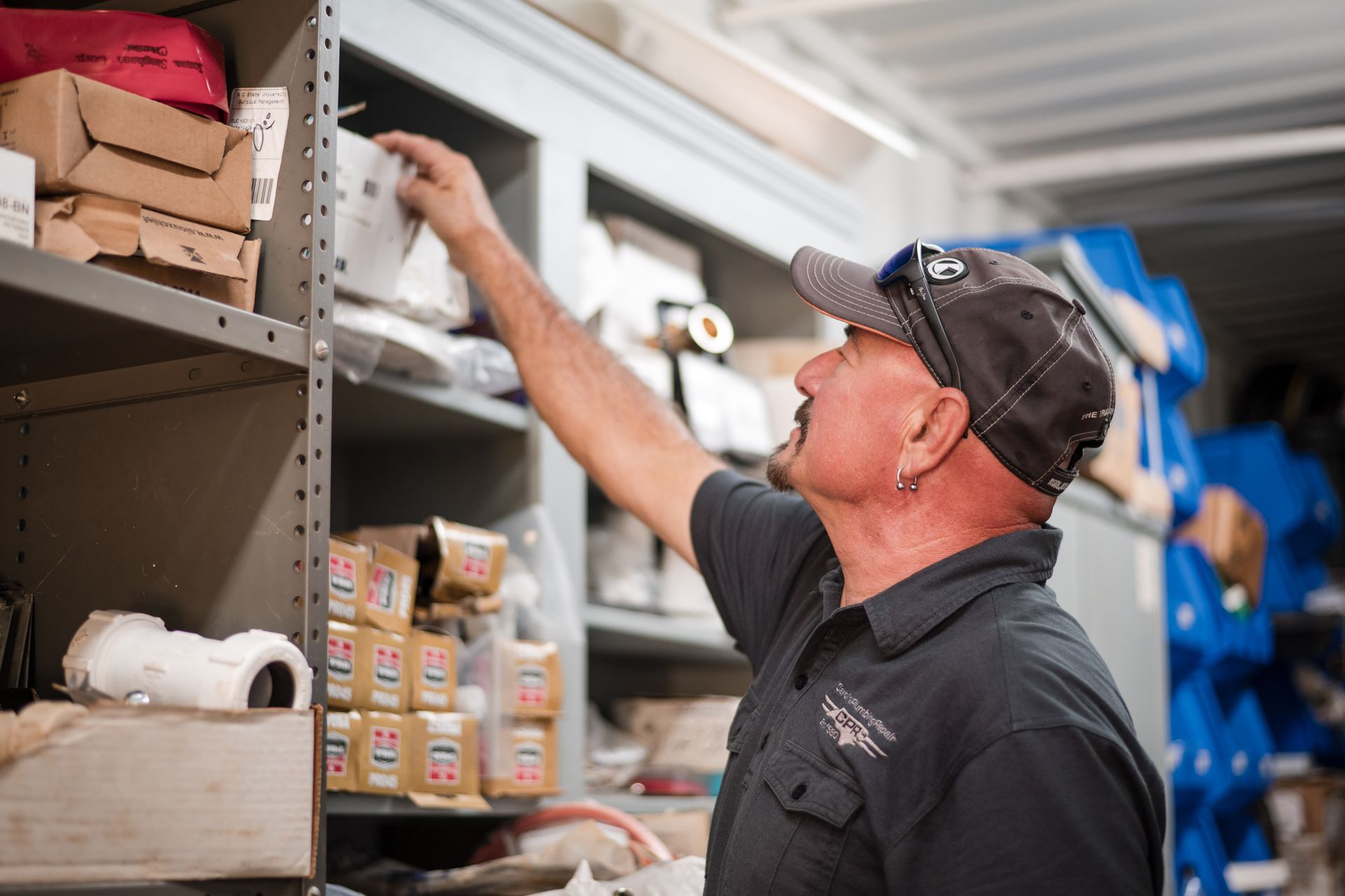 Man stocking shelves in a store aisle, reaching for items on a high shelf