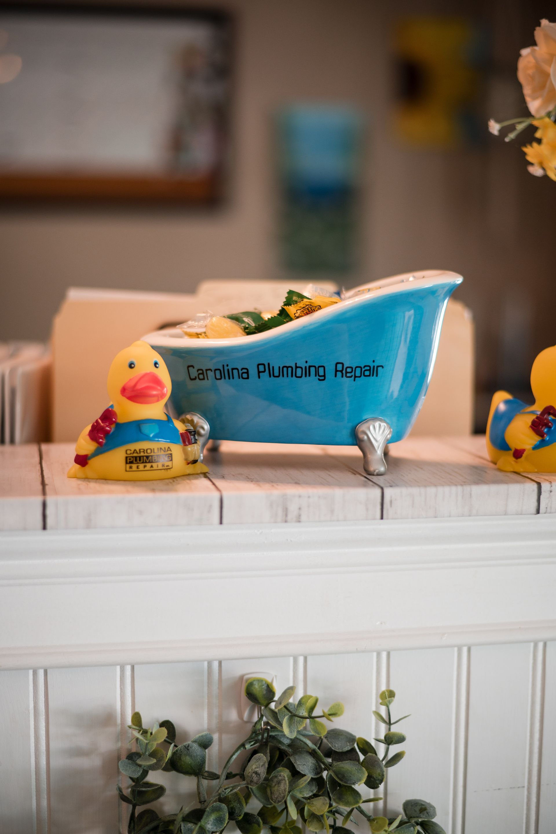Blue baby bathtub on a white shelf, flanked by rubber ducks in a softly blurred room.