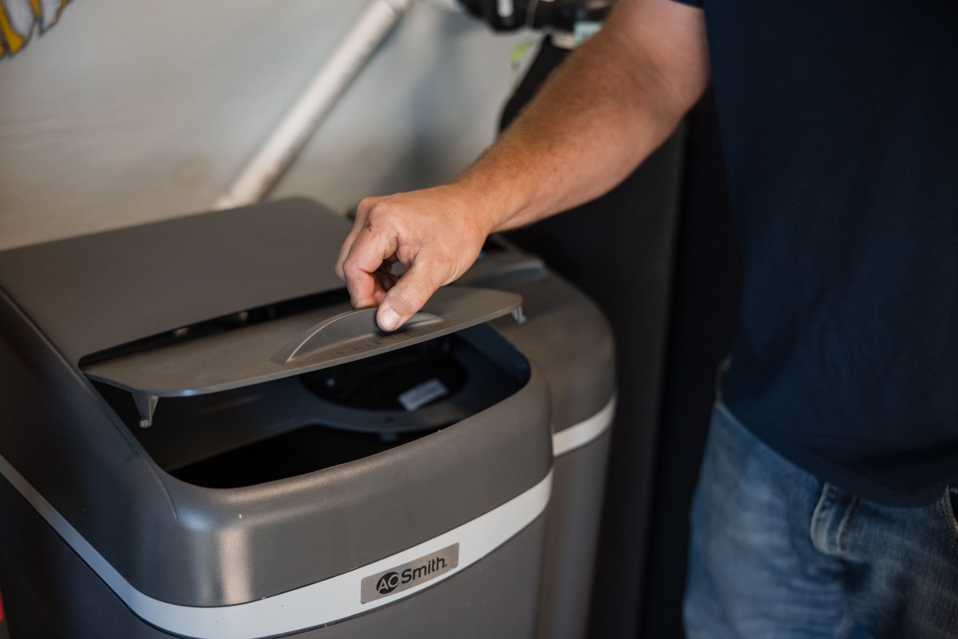 Hand opening a gray recycling bin to place paper inside