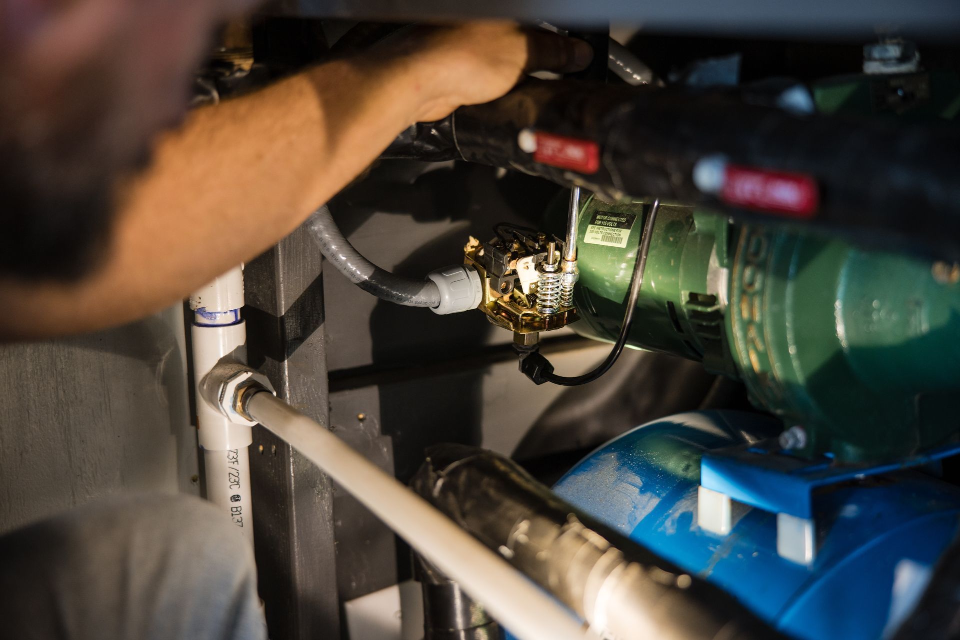 Worker adjusting machinery with a wrench beside green and blue industrial pipes