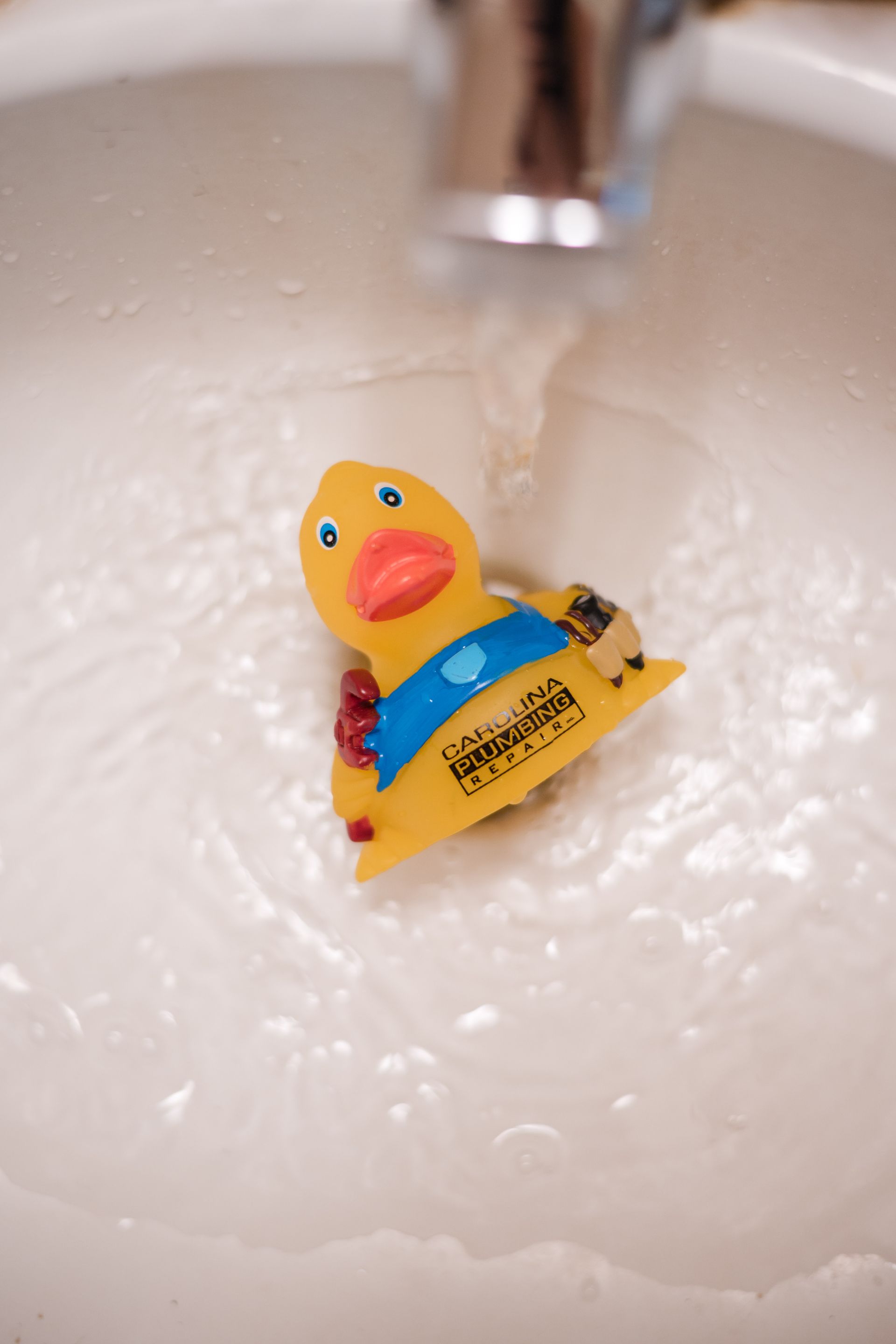 Yellow rubber duck under a running faucet in a sink full of water bubbles