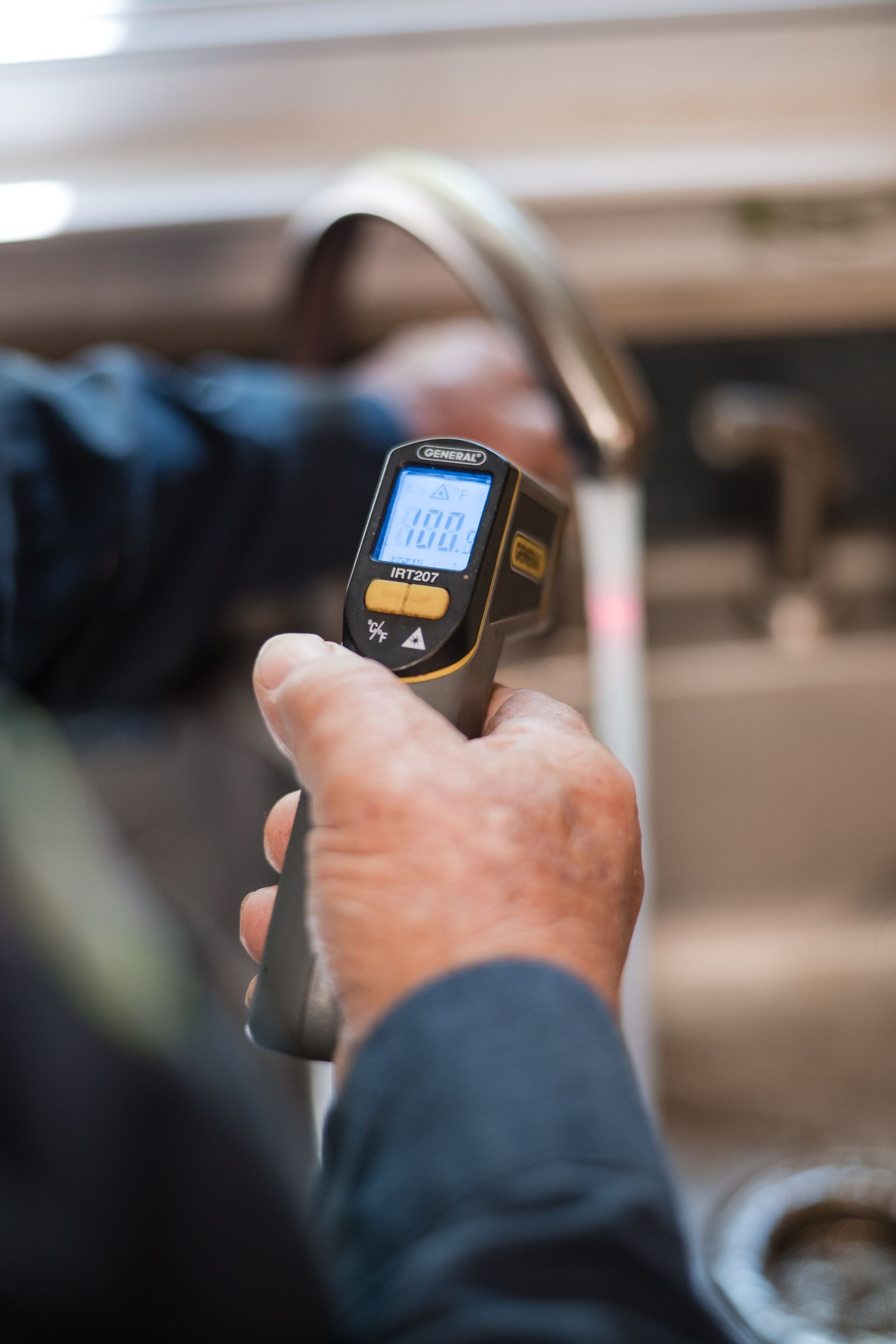 Hands using a handheld thermal scanner in a kitchen, aimed at a stove or pan.