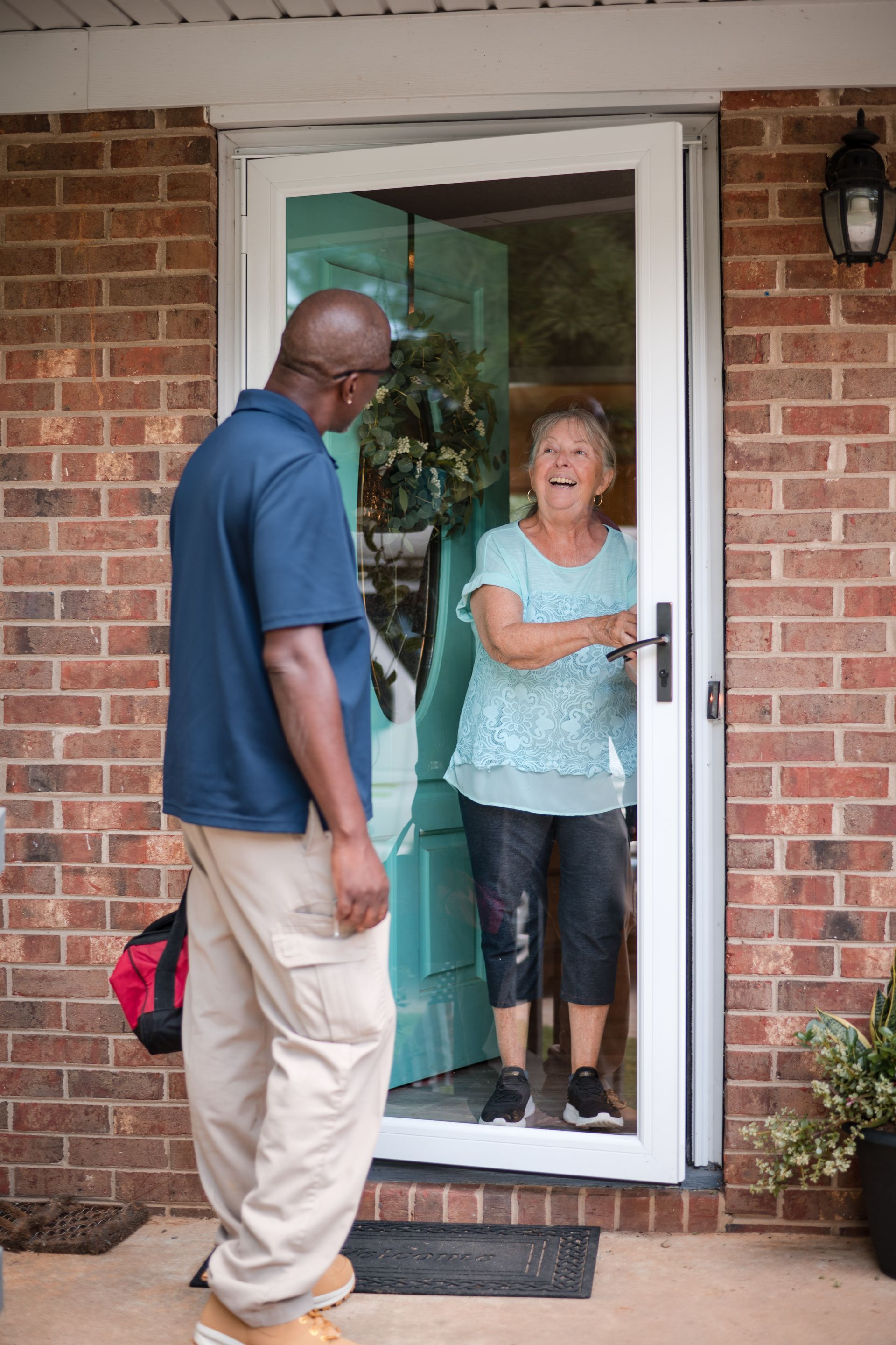 Two people at a front doorway, one inside smiling and holding the door open