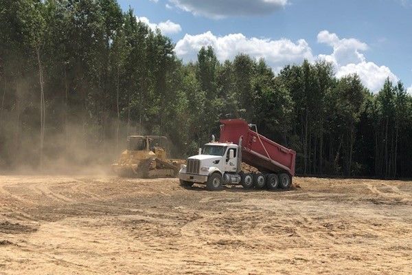 A dump truck is driving through a dirt field next to a bulldozer.