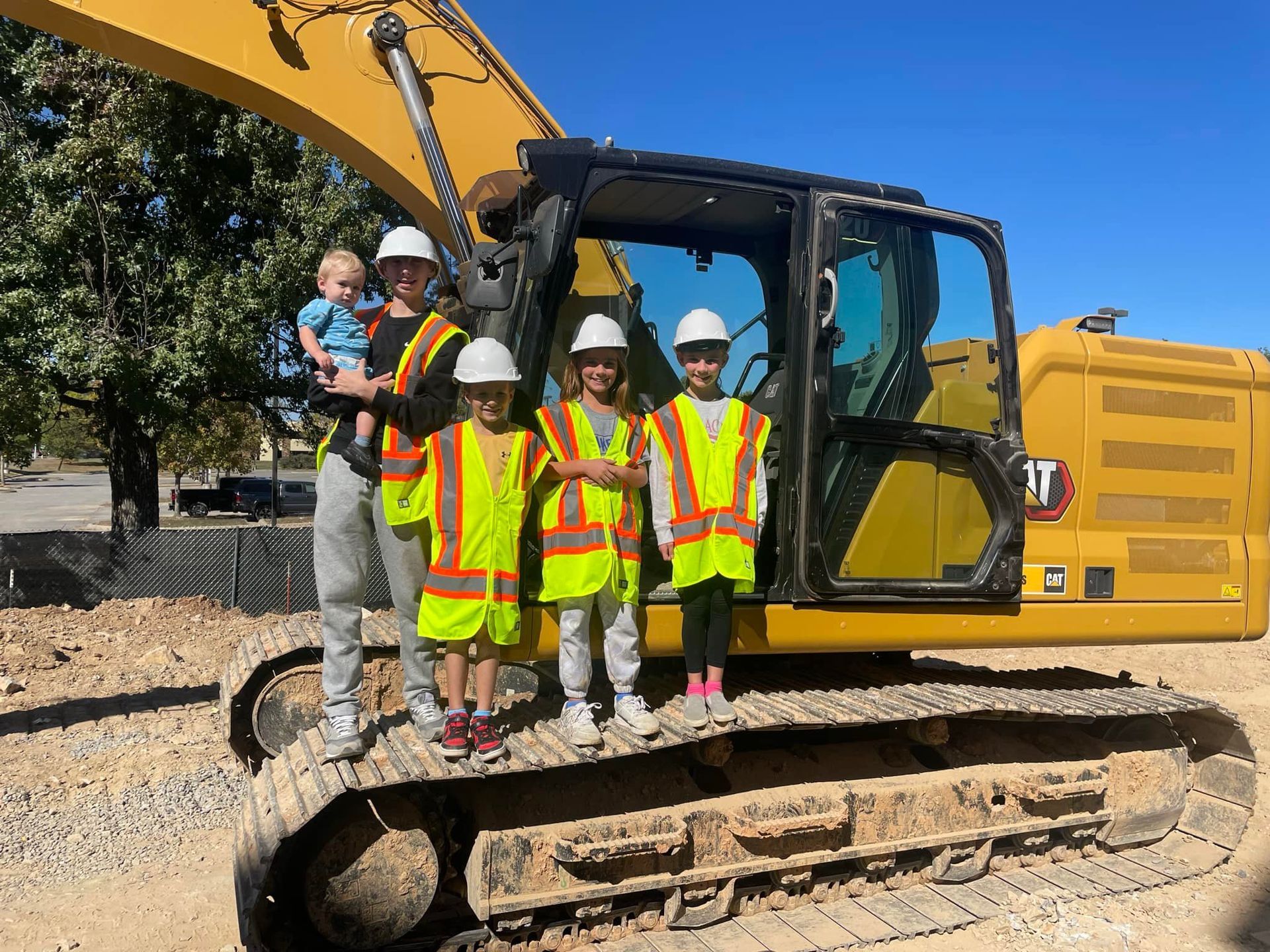 A group of children are standing next to a construction vehicle.