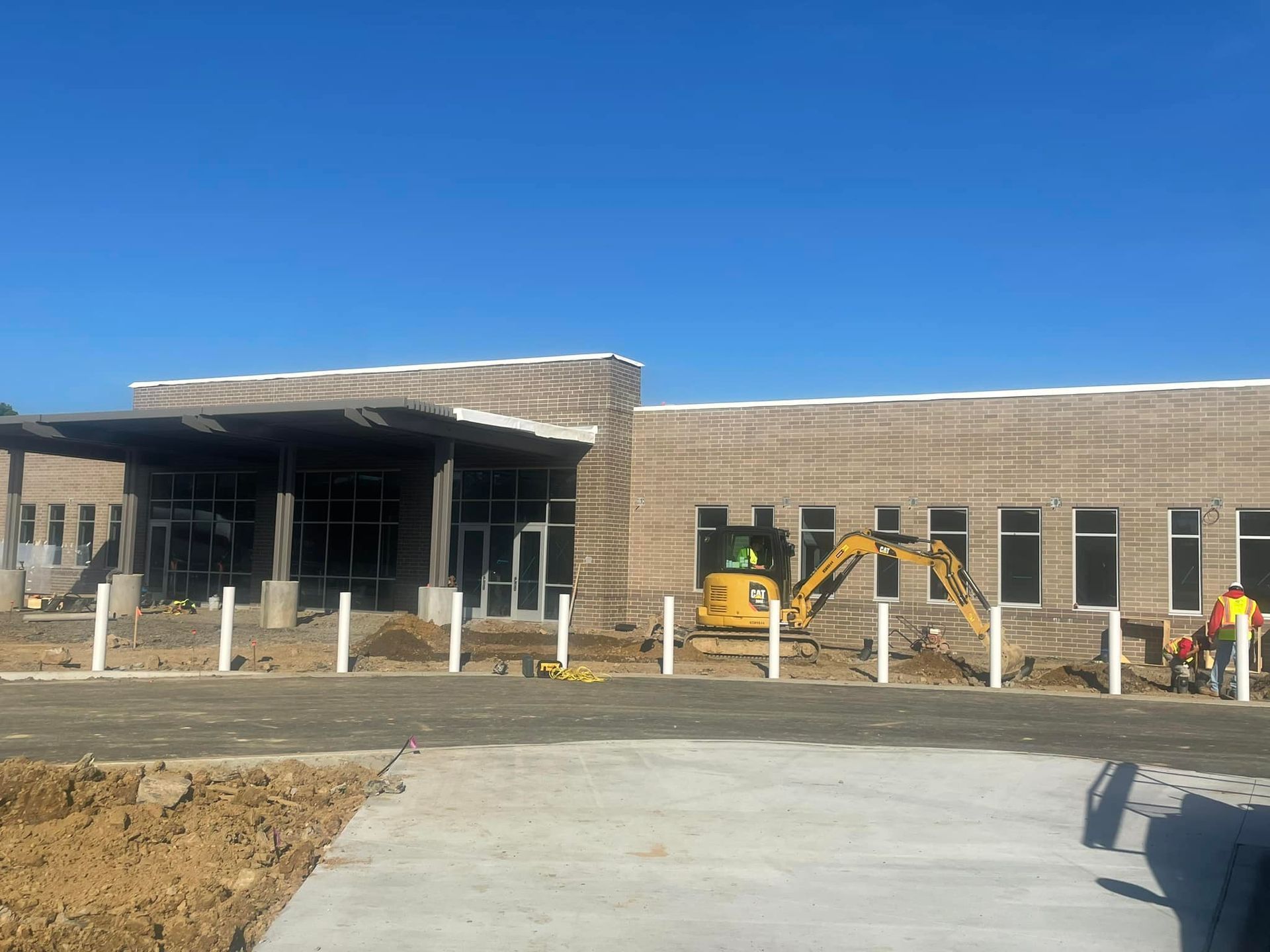 A large building under construction with a yellow excavator in front of it.