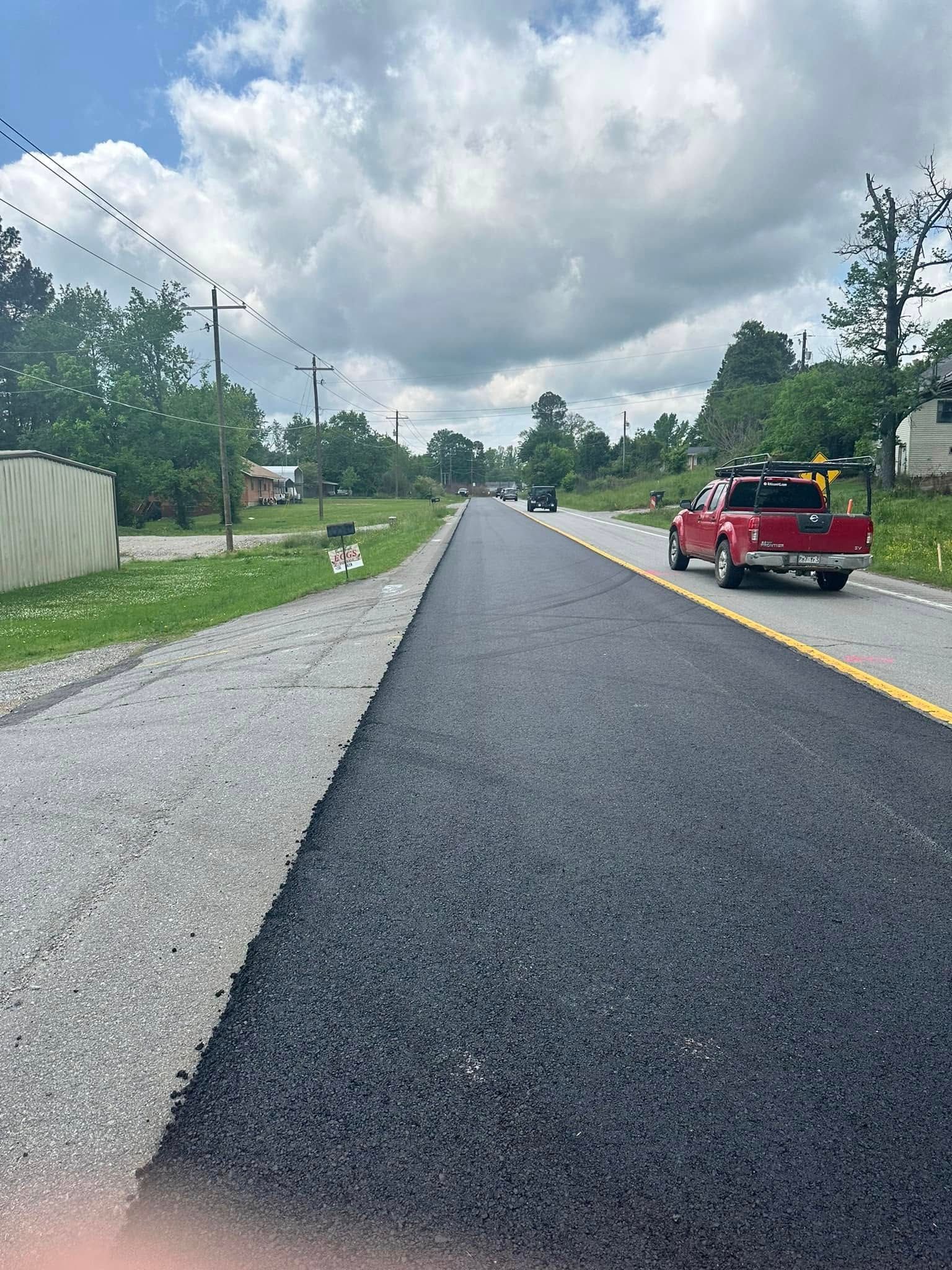 A red truck is driving down a newly paved road.
