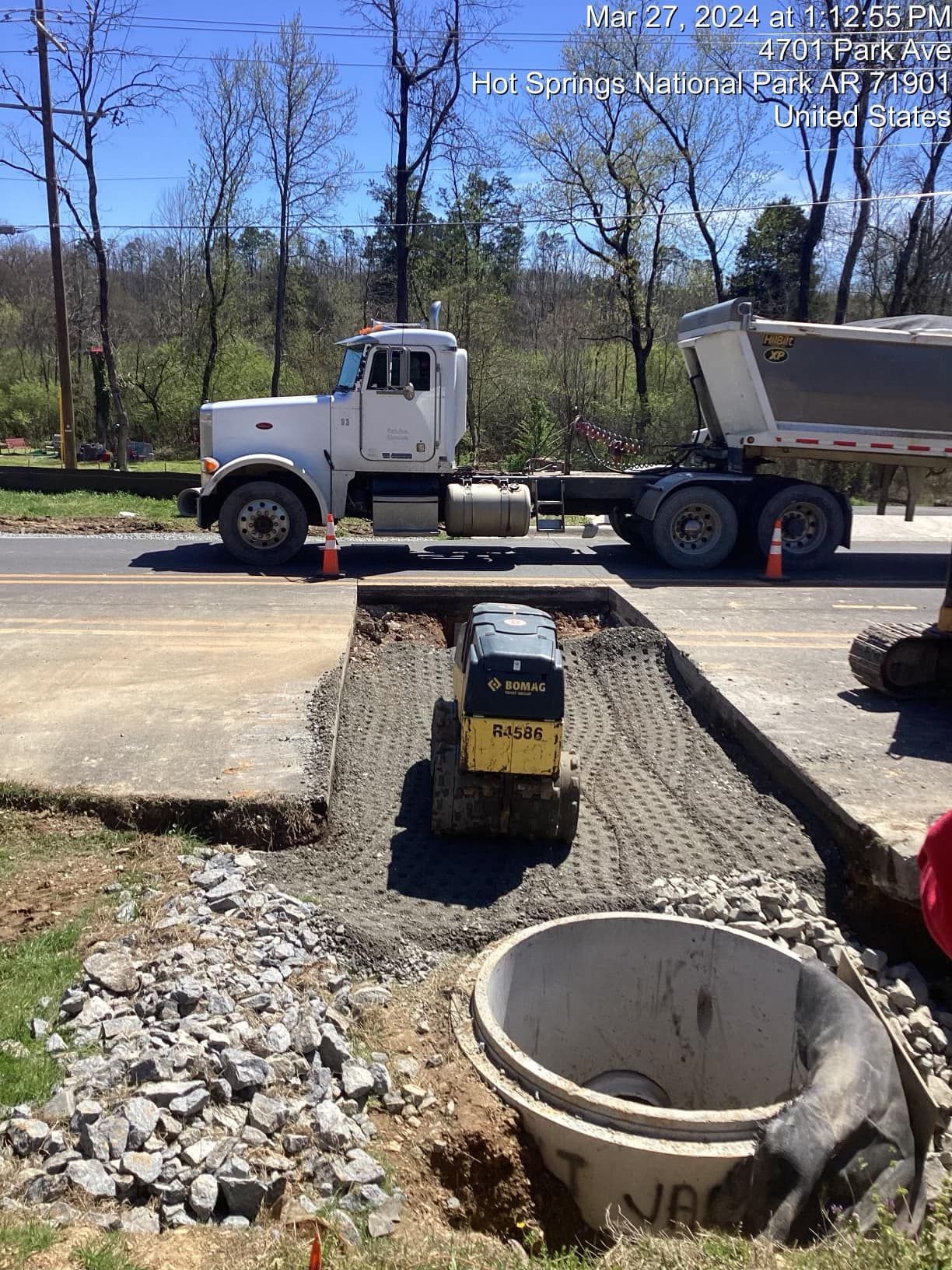 A dump truck is parked on the side of the road next to a small bulldozer.