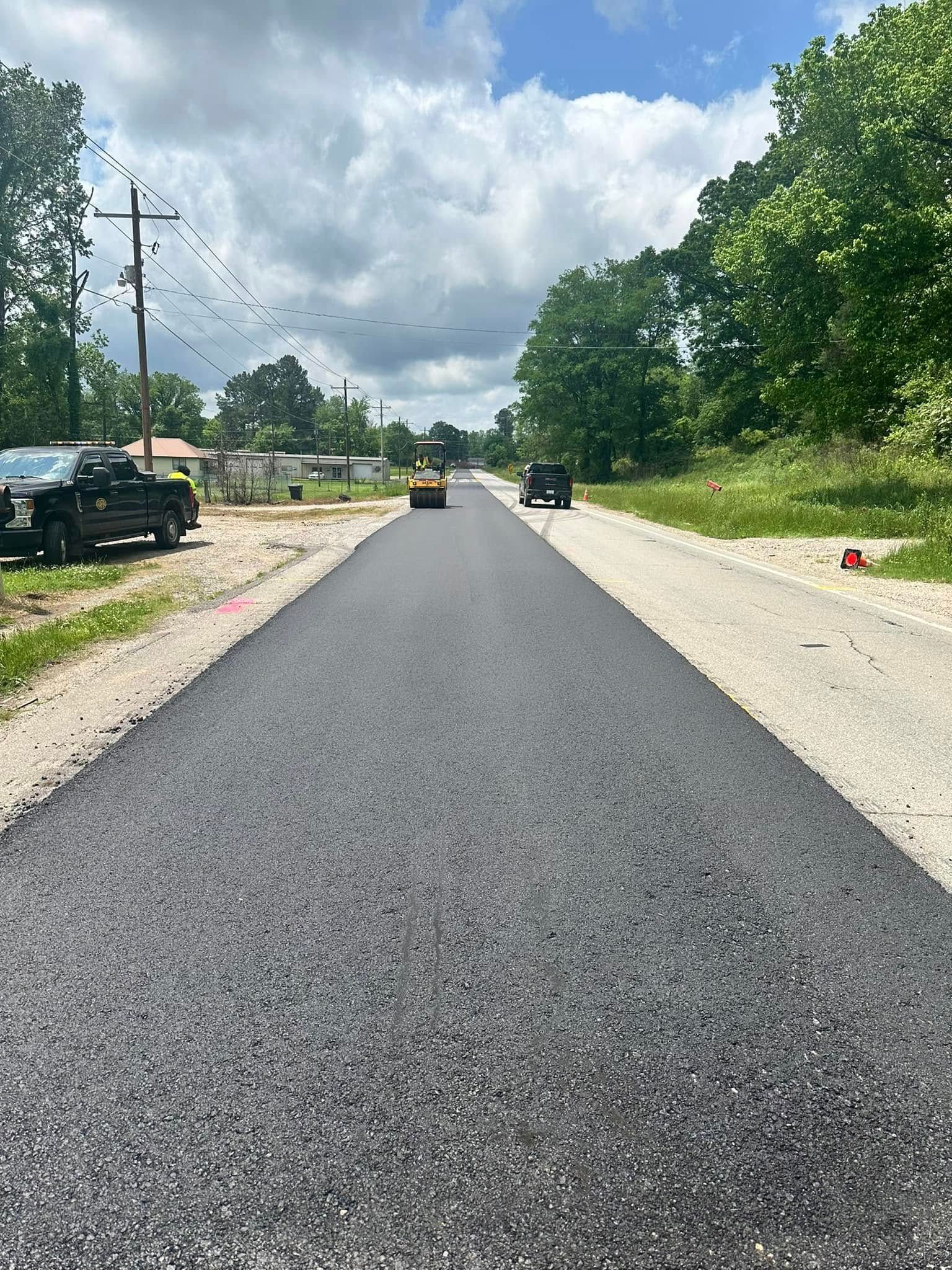 A black truck is driving down a newly paved road.