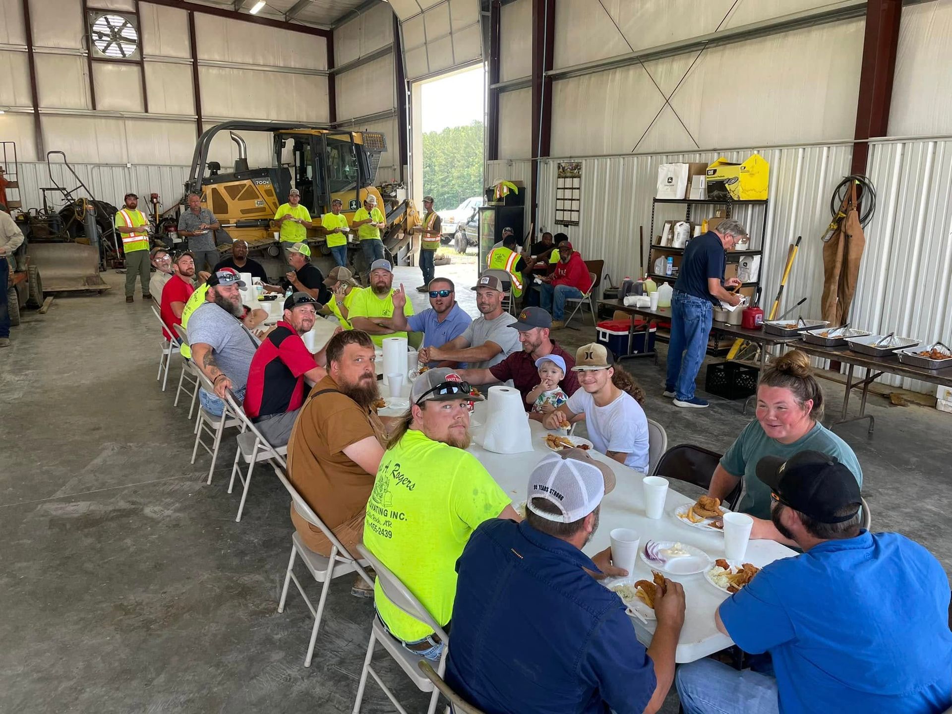 A group of people are sitting at tables in a warehouse eating food.