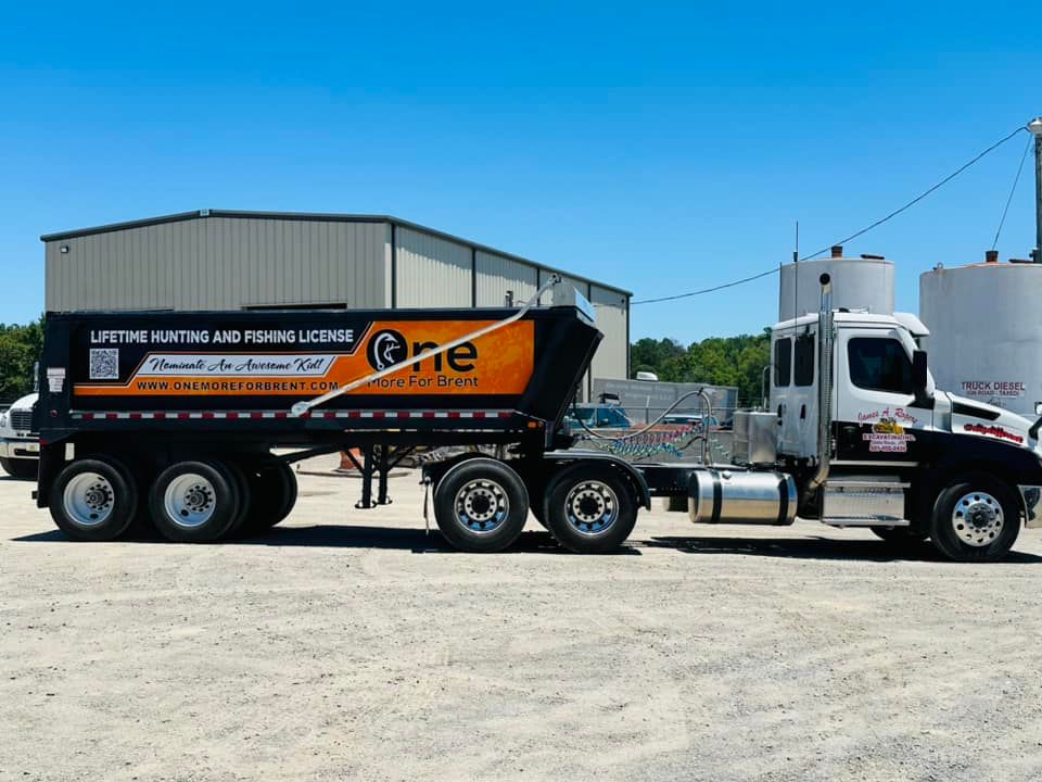 A dump truck is parked in a dirt lot in front of a building.