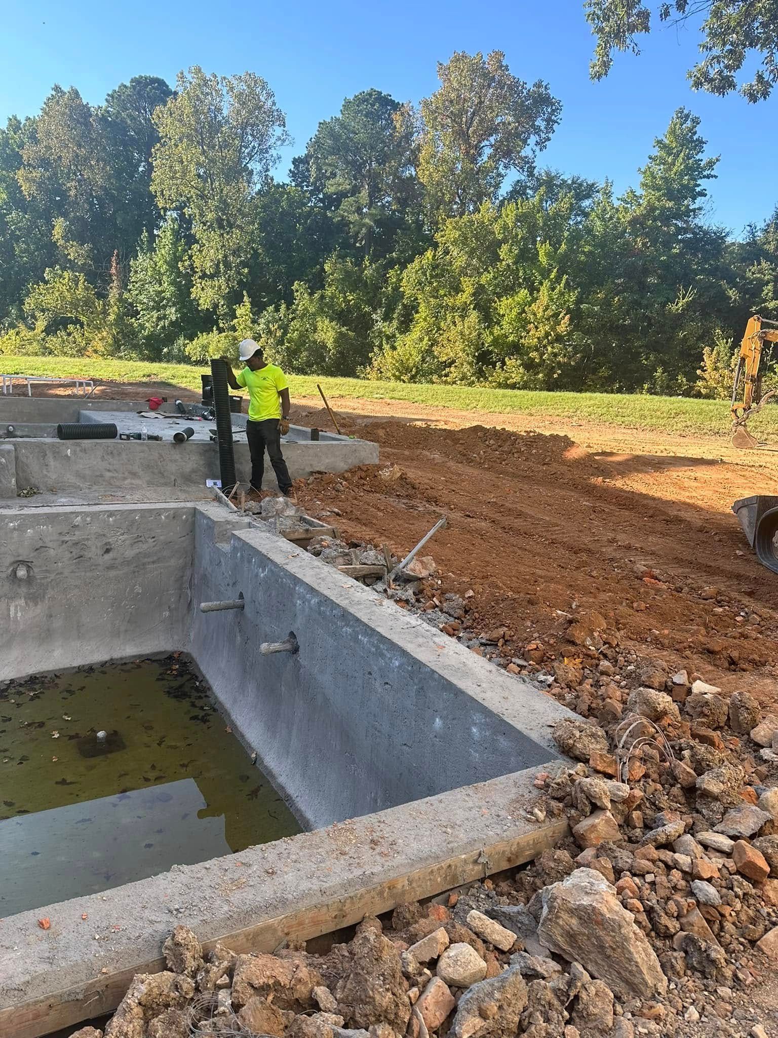 A man is standing next to a pool in a dirt field.