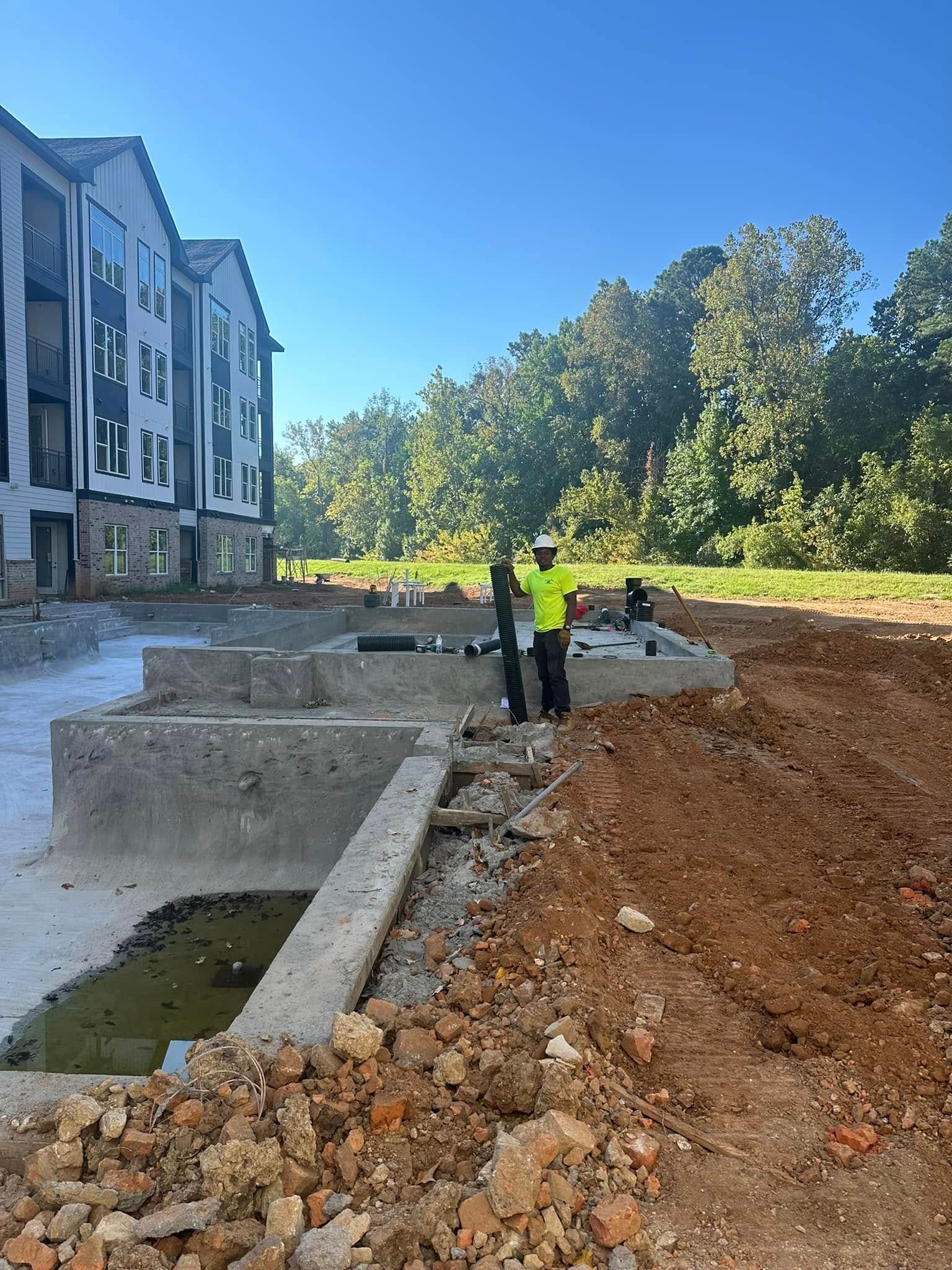 A man in a yellow vest is standing in a dirt field in front of a building under construction.
