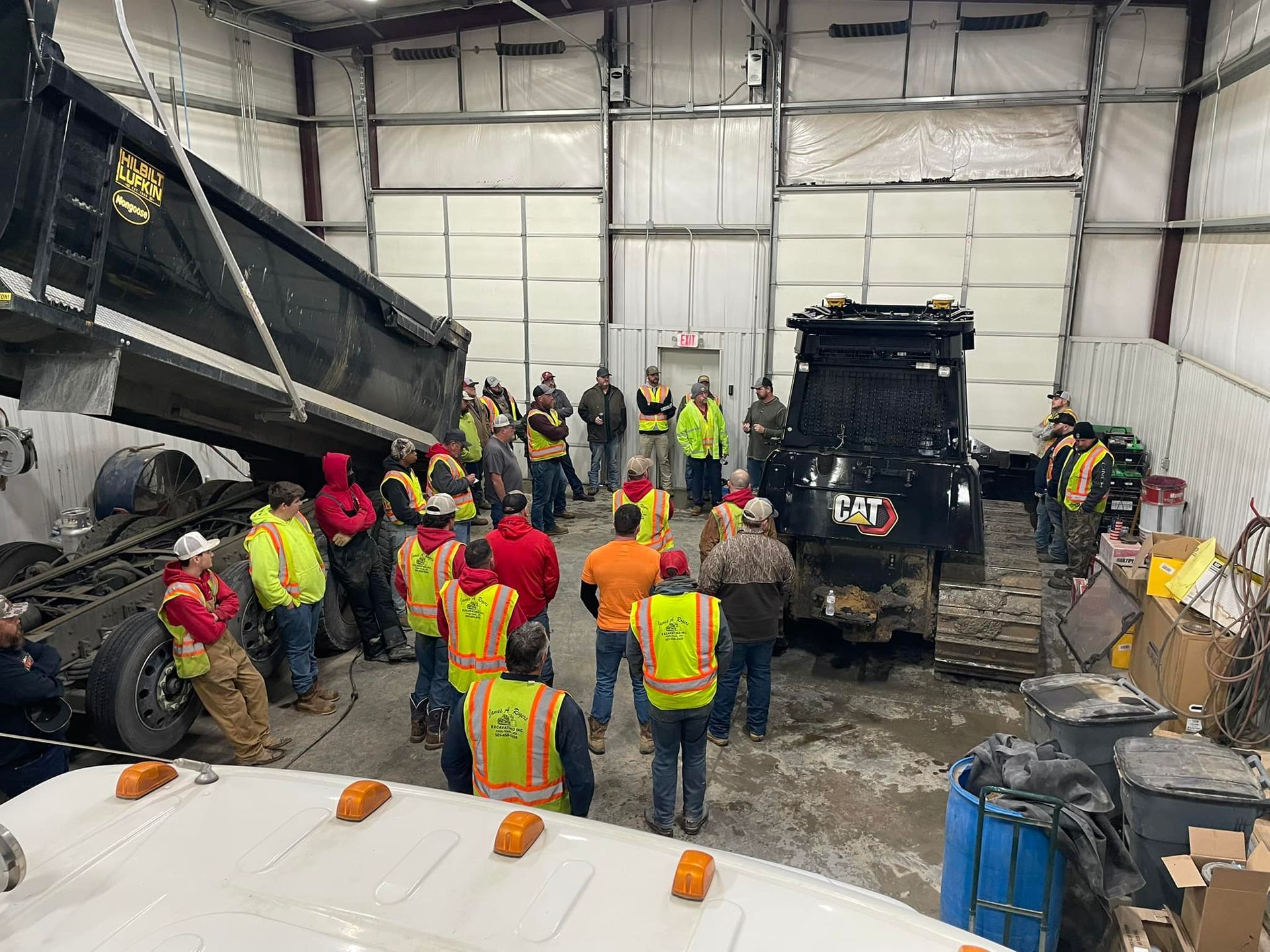 A group of construction workers are standing around a dump truck in a garage.