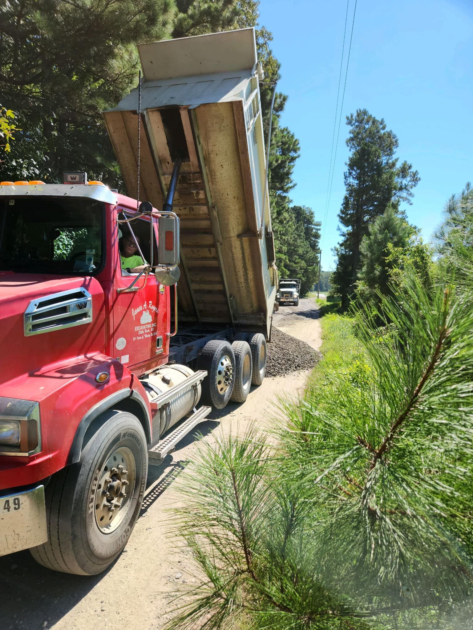A red dump truck is driving down a dirt road.