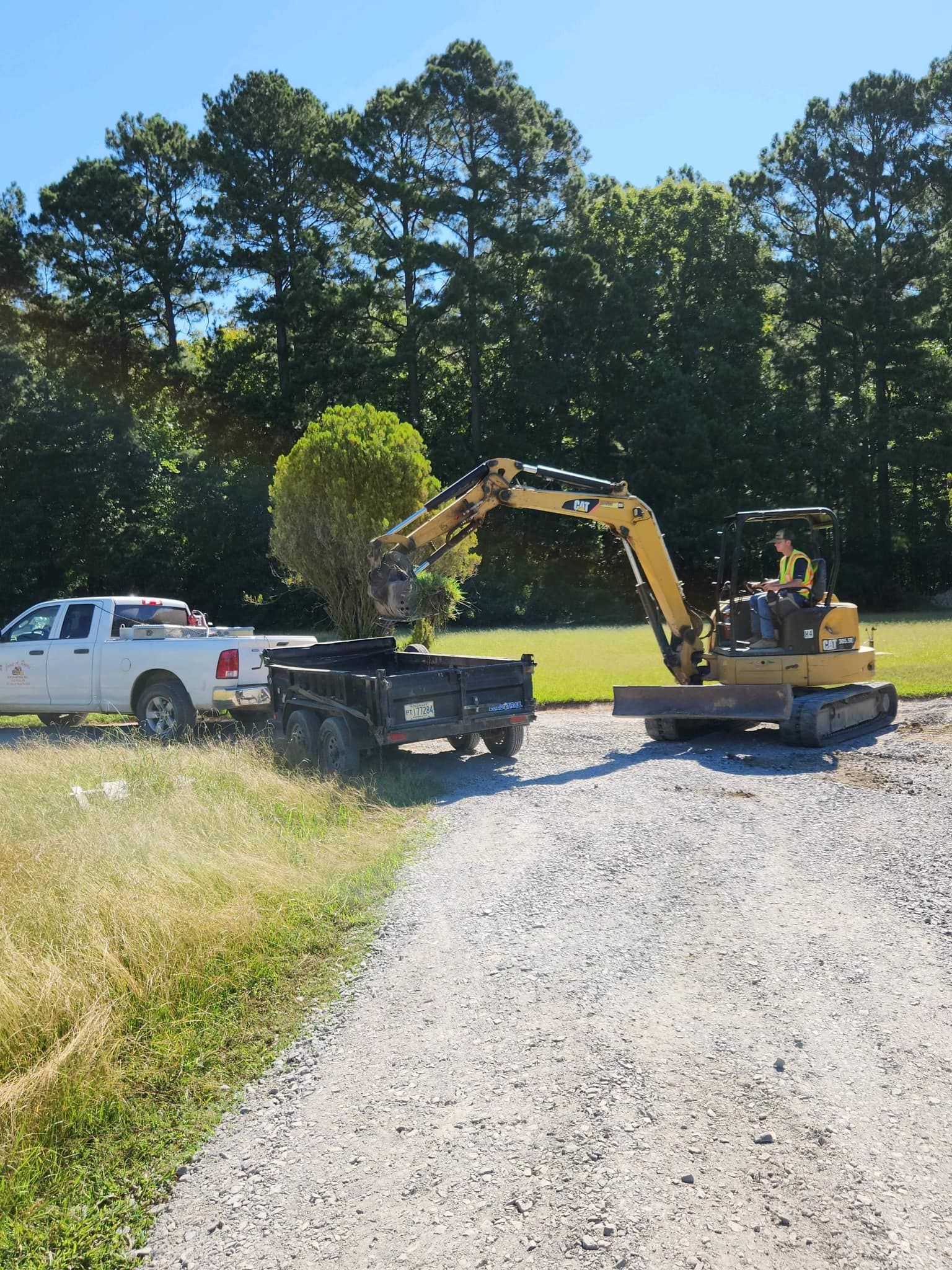 A white truck is being towed by an excavator with a tree in the back.