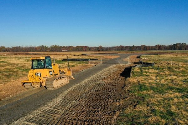 A bulldozer is driving down a dirt road in a field.