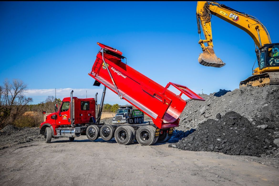 A red dump truck is being loaded with dirt by a yellow excavator.