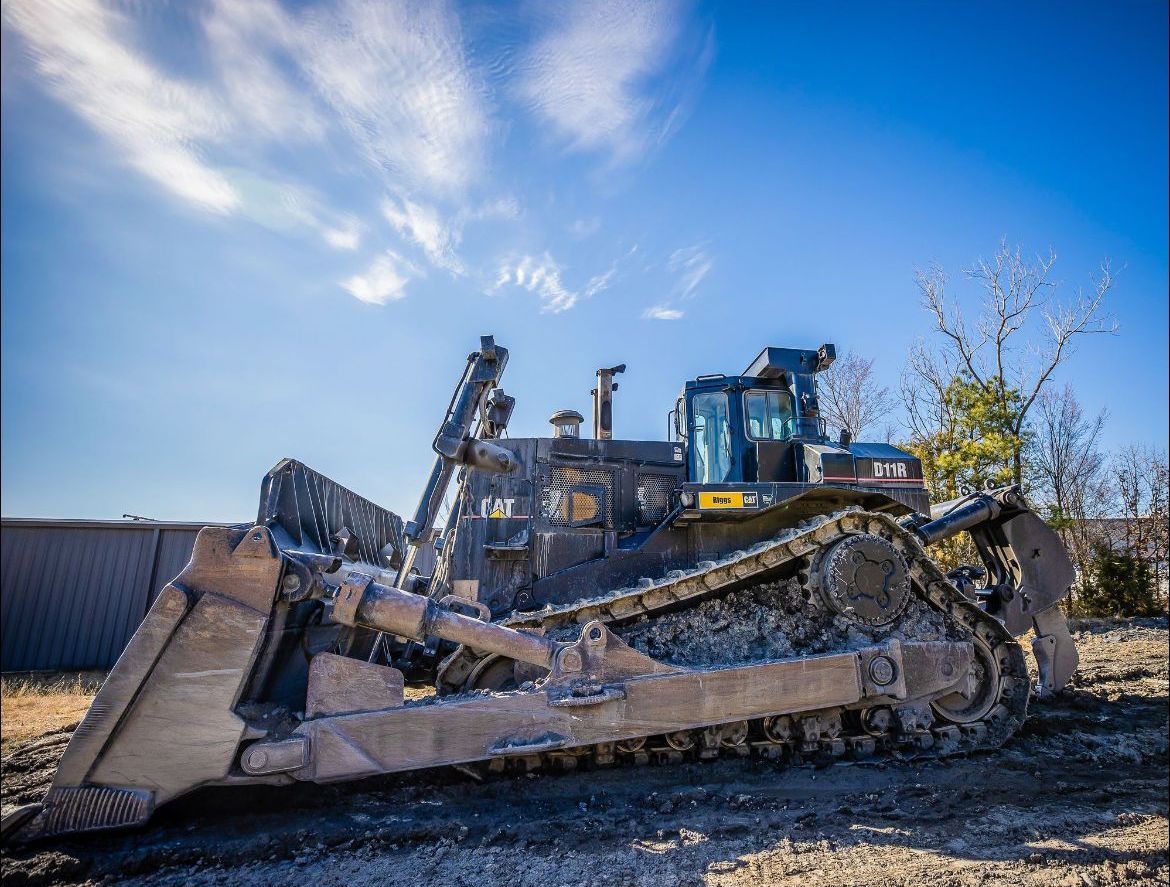A bulldozer is parked in a dirt field with a blue sky in the background.
