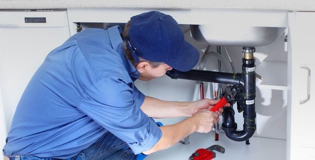 Plumber fixing a pipe under a kitchen sink