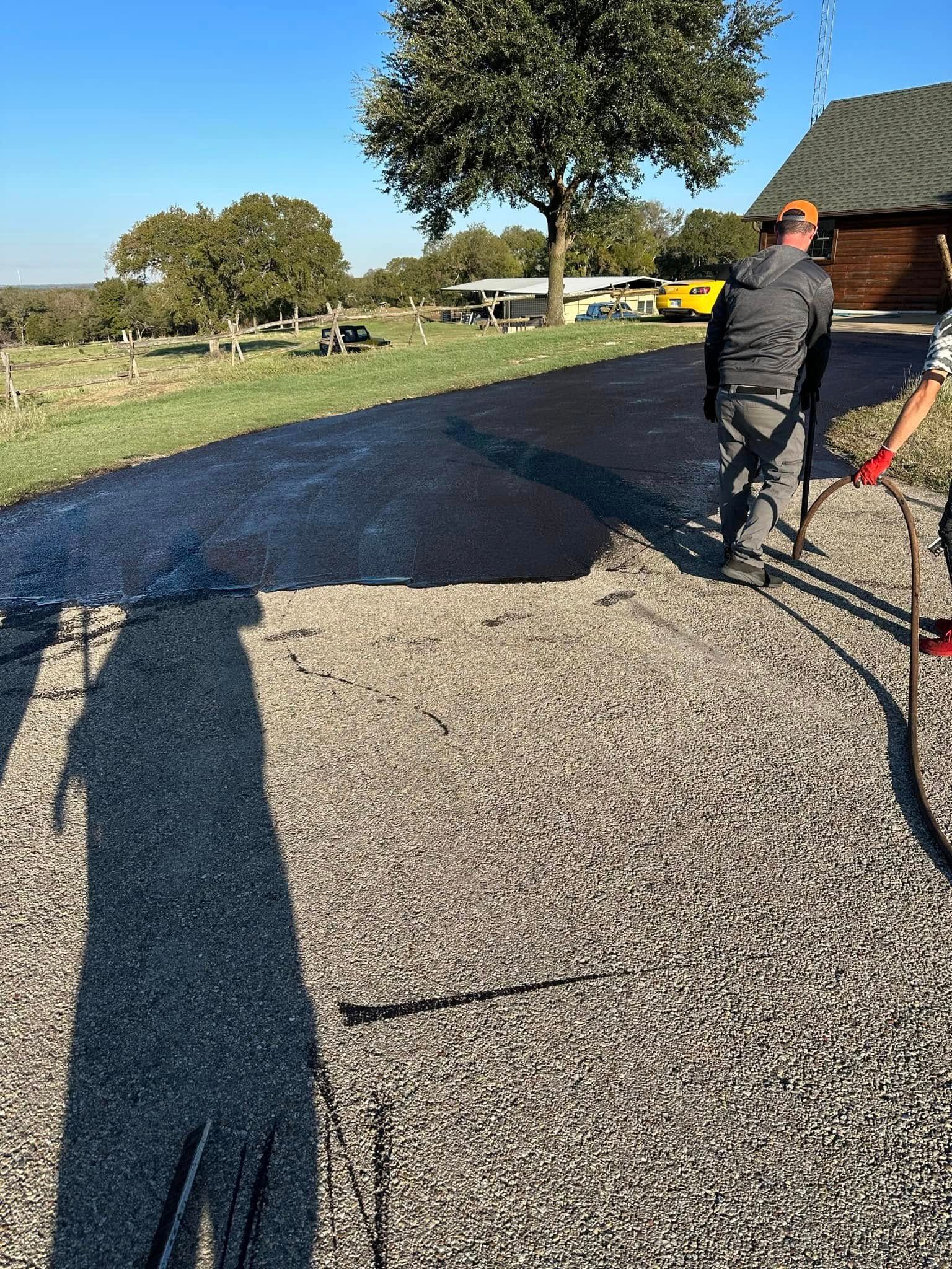 Workers in blue uniforms spread asphalt on a road surface using shovels.