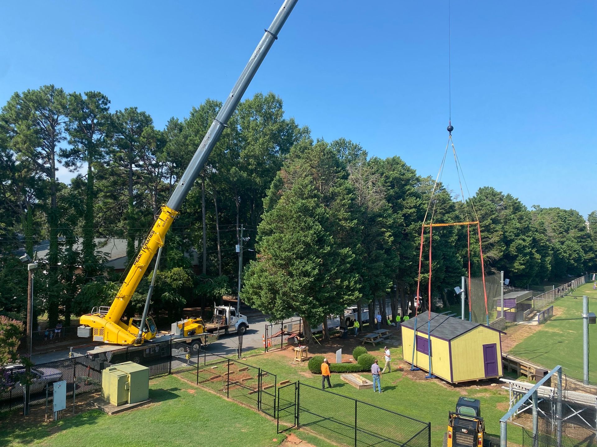 A crane is lifting a shed in a park.