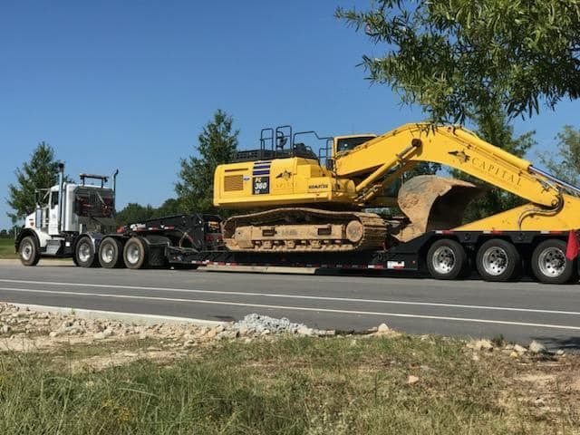 A truck is carrying a large yellow excavator on a trailer.
