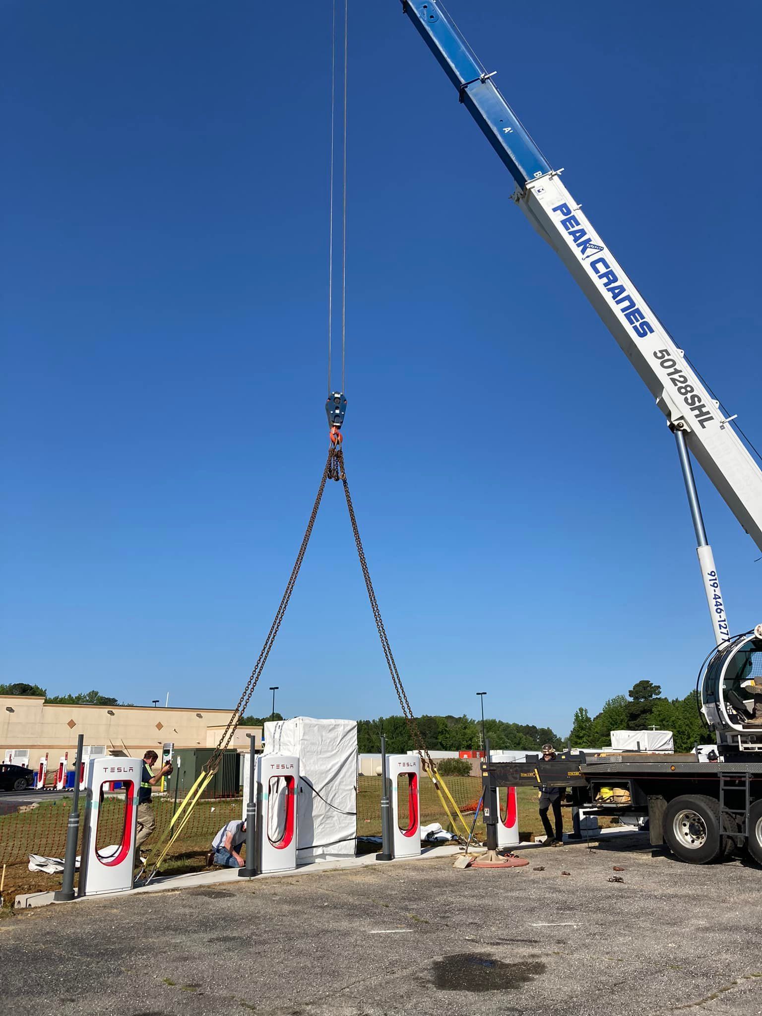 A crane is lifting a tesla charging station in a parking lot.