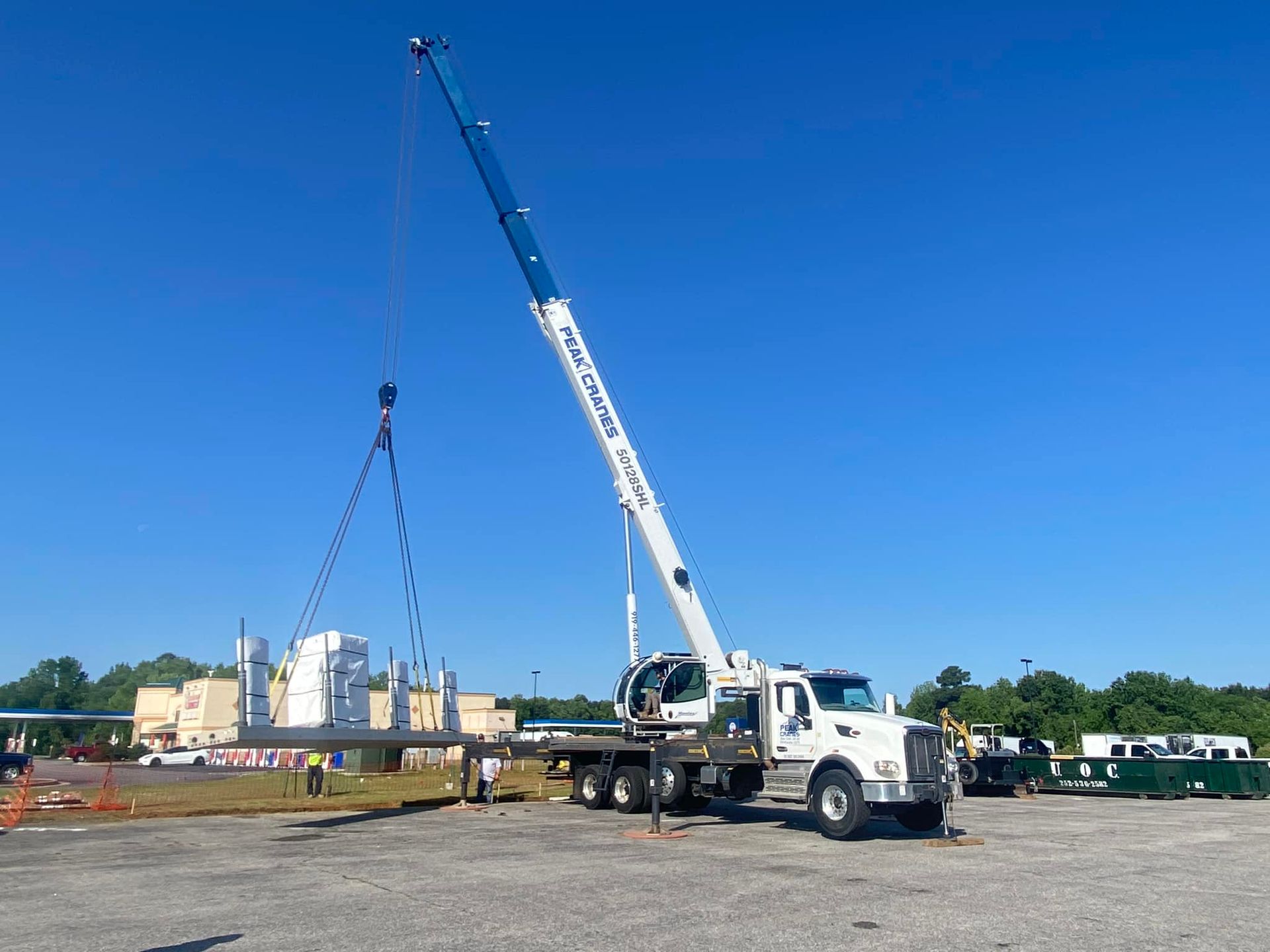A large crane is lifting a large piece of metal in a parking lot.