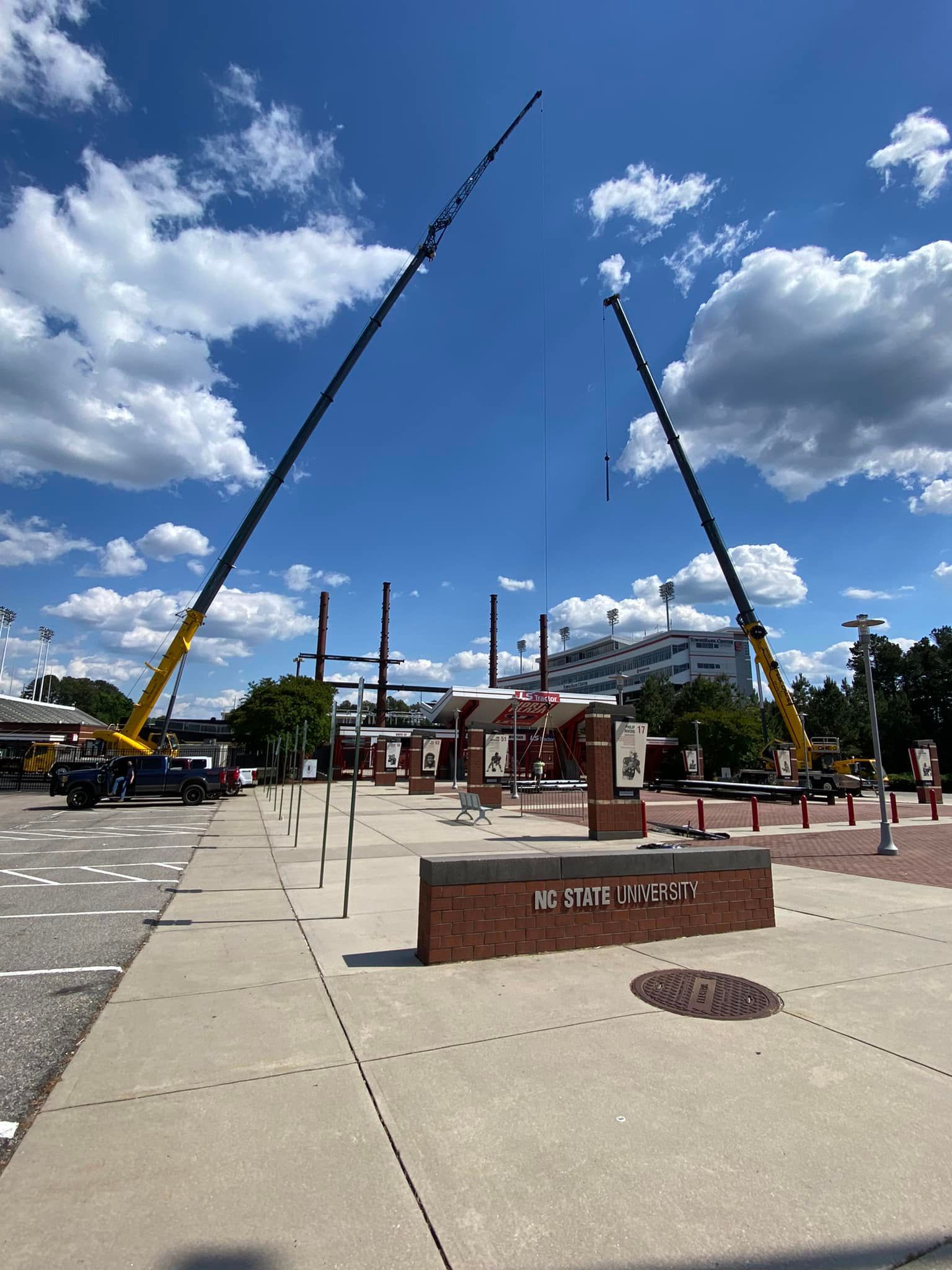 Two cranes are being used to lift a statue in a park