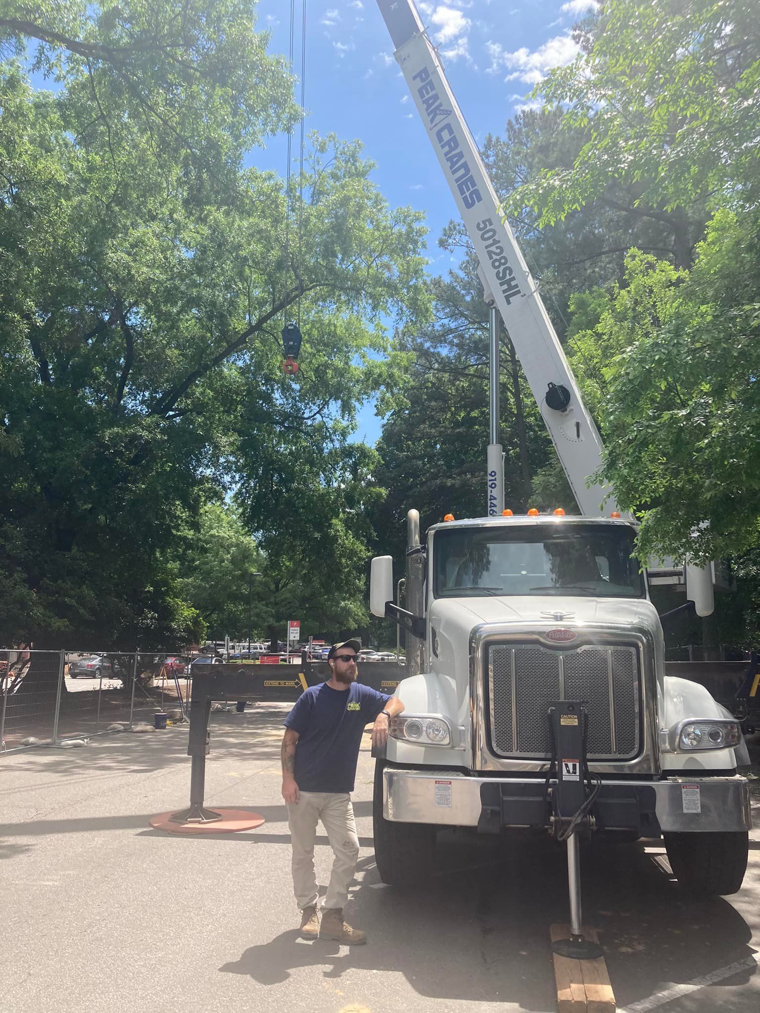 A man is standing next to a crane truck in a parking lot.