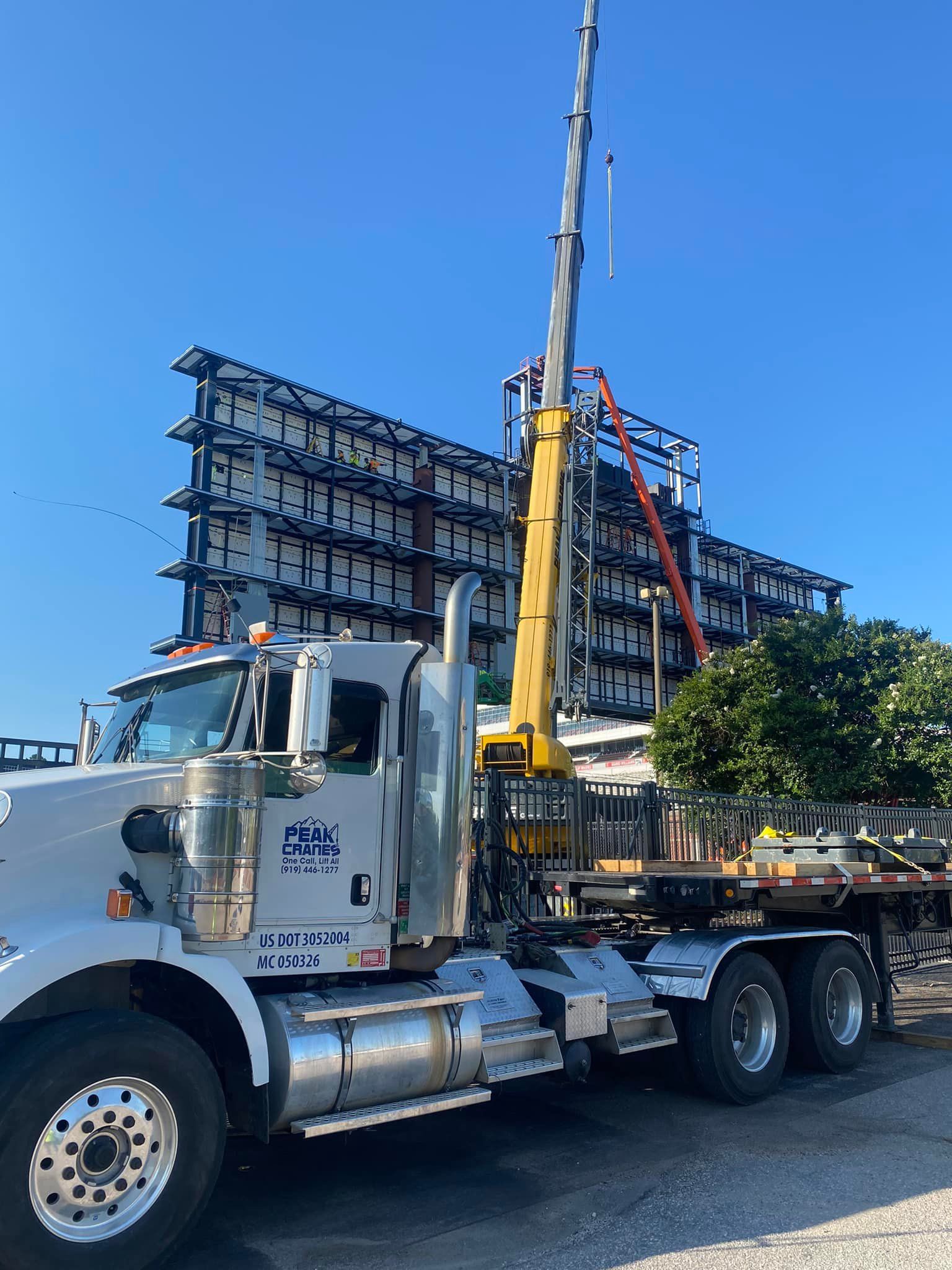 A semi truck with a crane attached to it is parked in front of a building under construction.