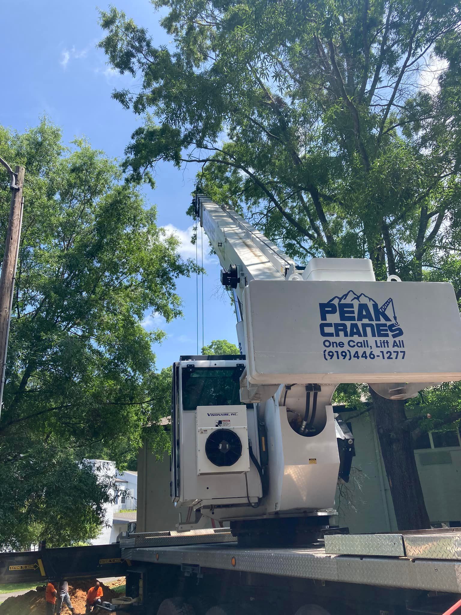 A crane is sitting on top of a truck next to a tree.