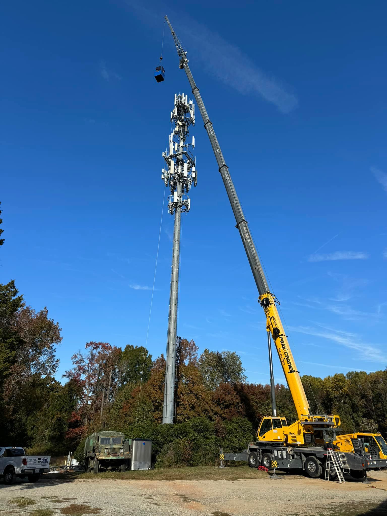 A large yellow crane is lifting a cell phone tower